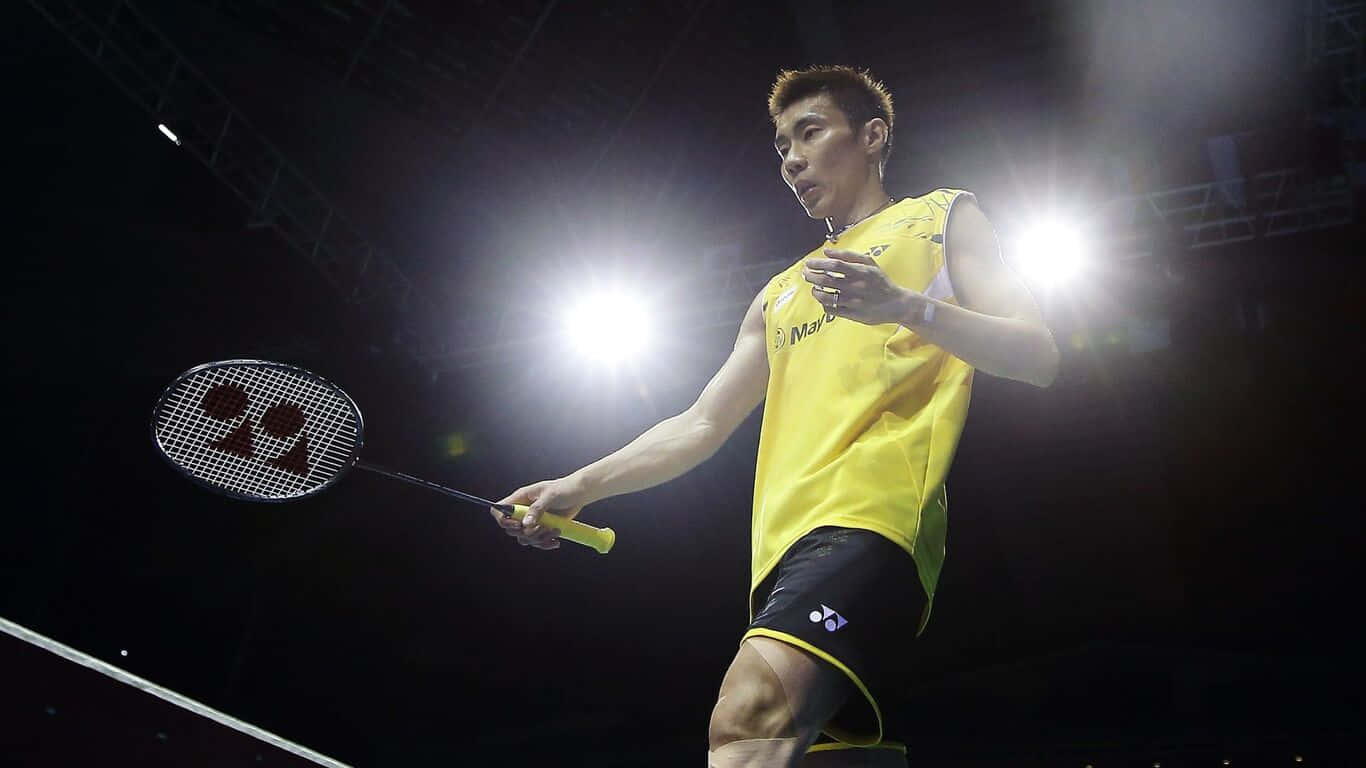1366x768 Badminton 桌布 壁紙 — 一名身穿黃色球衣的羽球運動員在明亮的場館燈光下，在黑暗背景中揮拍。