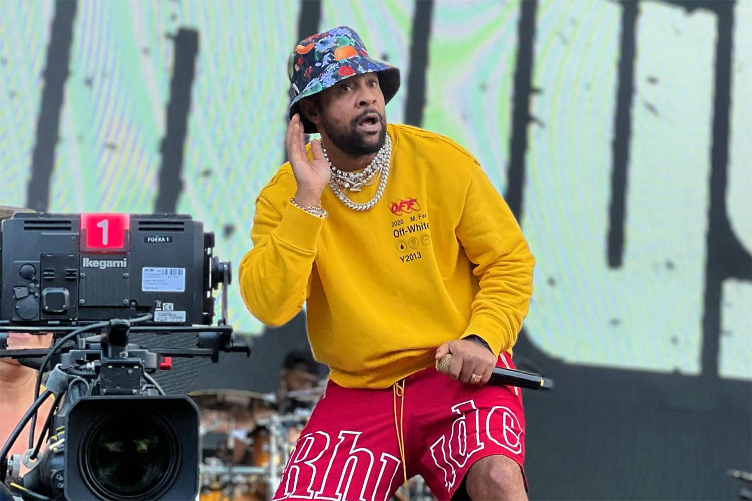 Rappers 桌布 壁紙 — 一名身穿黃色衛衣和紅色短褲的男子在舞台上表演，前景有一部相機。