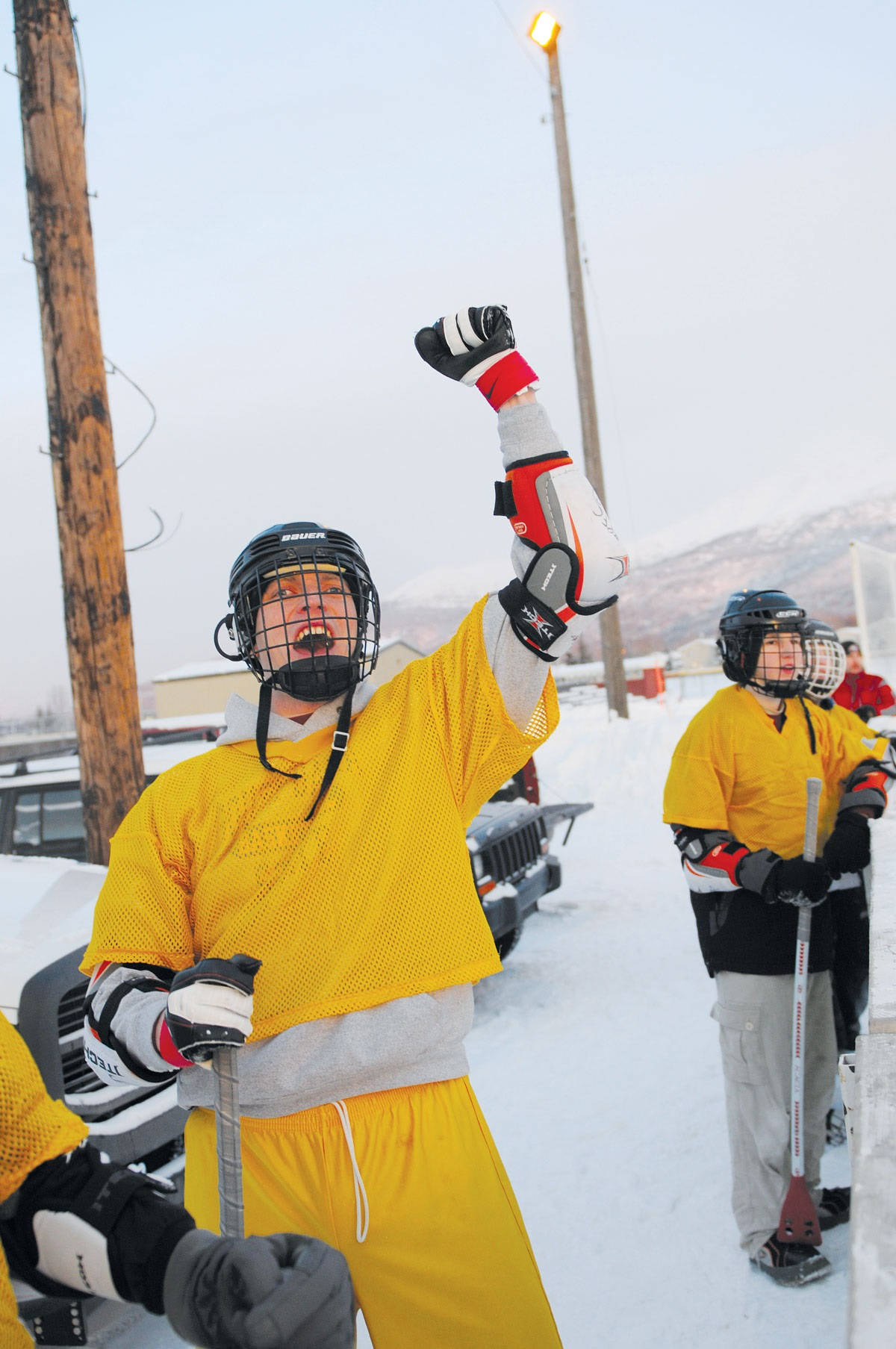 運動 桌布 壁紙 — 一名身穿黃色裝備的曲棍球運動員在雪白的冬日空氣中勝利地舉起戴著手套的拳頭，隊友們站在附近。