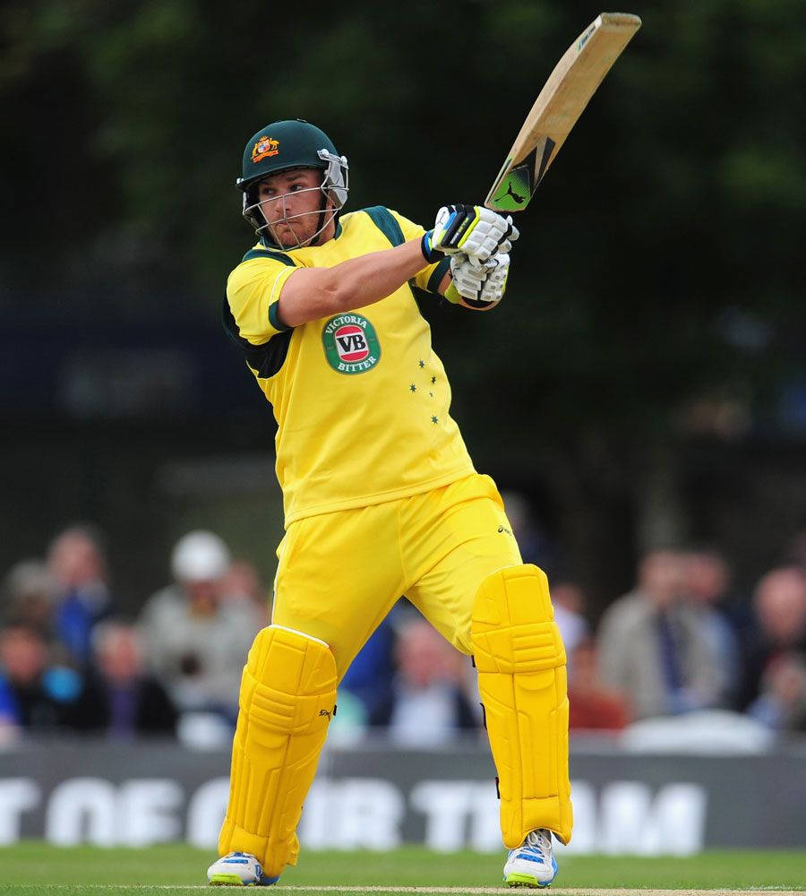 Aaron Finch 桌布 壁紙 — 一名身穿黃色裝備的板球擊球手在綠色場地上揮動球棒，背景有模糊的觀眾。