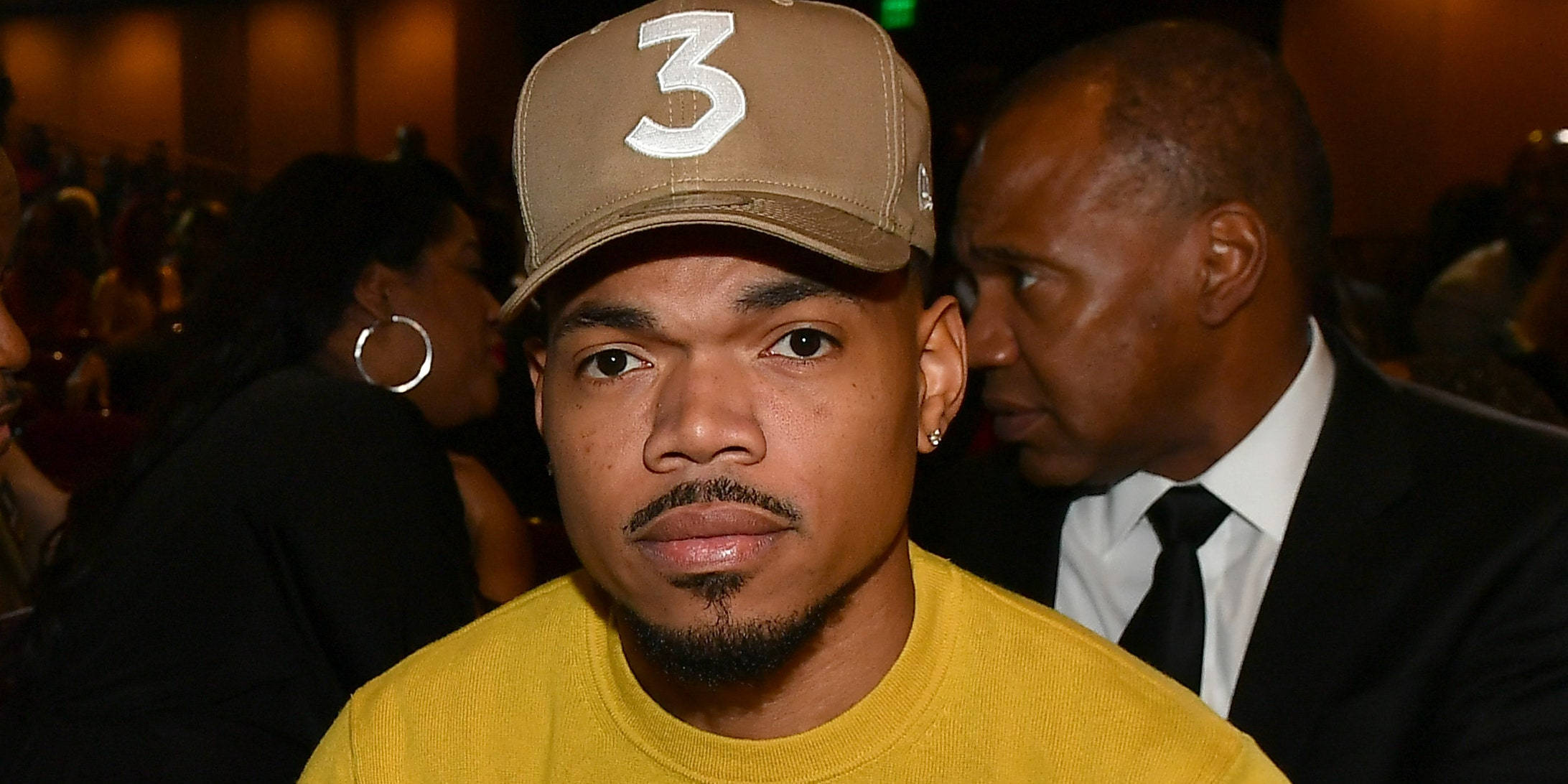 chance 桌布 壁紙 — 一名身穿黃色襯衫、戴著米色帽子、帽上有白色數字三的男子，在昏暗的室內環境中直視鏡頭。