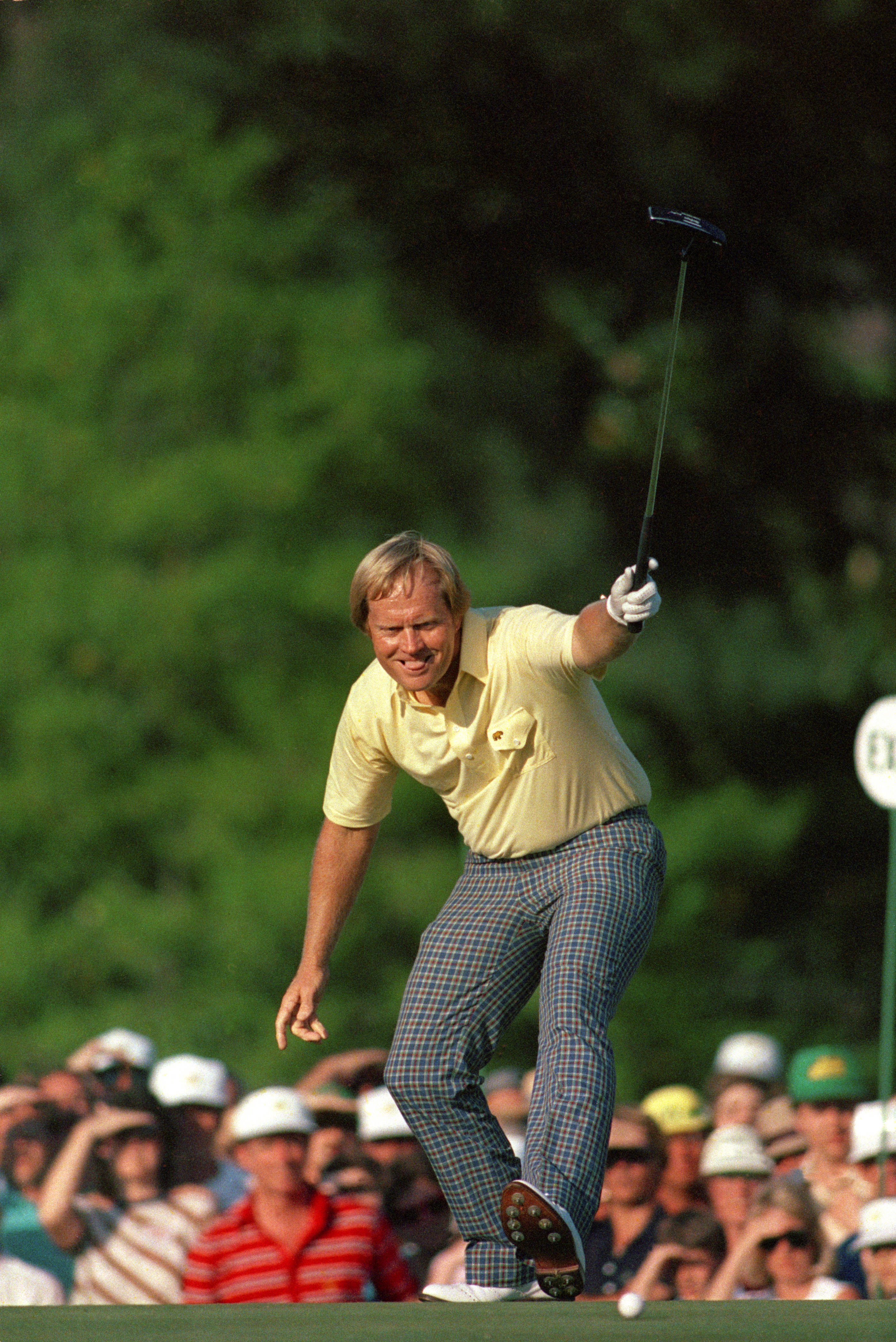 桌布 壁紙 — 一名身穿黃色襯衫和格子褲的高爾夫球手在陽光明媚的果嶺上勝利慶祝，周圍有群眾觀看。