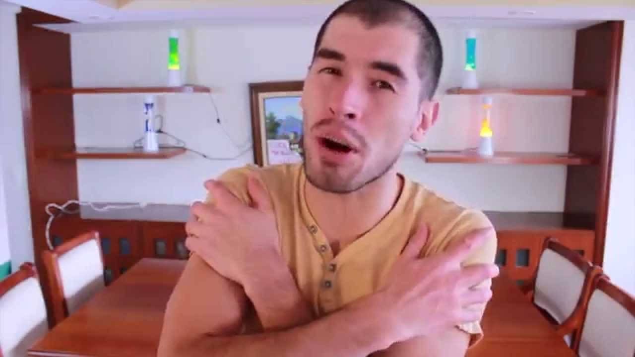 搞笑 桌布 壁紙 — 一名身穿黃色襯衫的男子在一個有木製家具和發光熔岩燈的飯廳中雙臂交叉放在胸前。