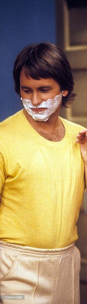 John Ritter 桌布 壁紙 — 一名身穿黃色襯衫的男子在攝影棚環境中，專注地將刮鬍膏塗在臉上。