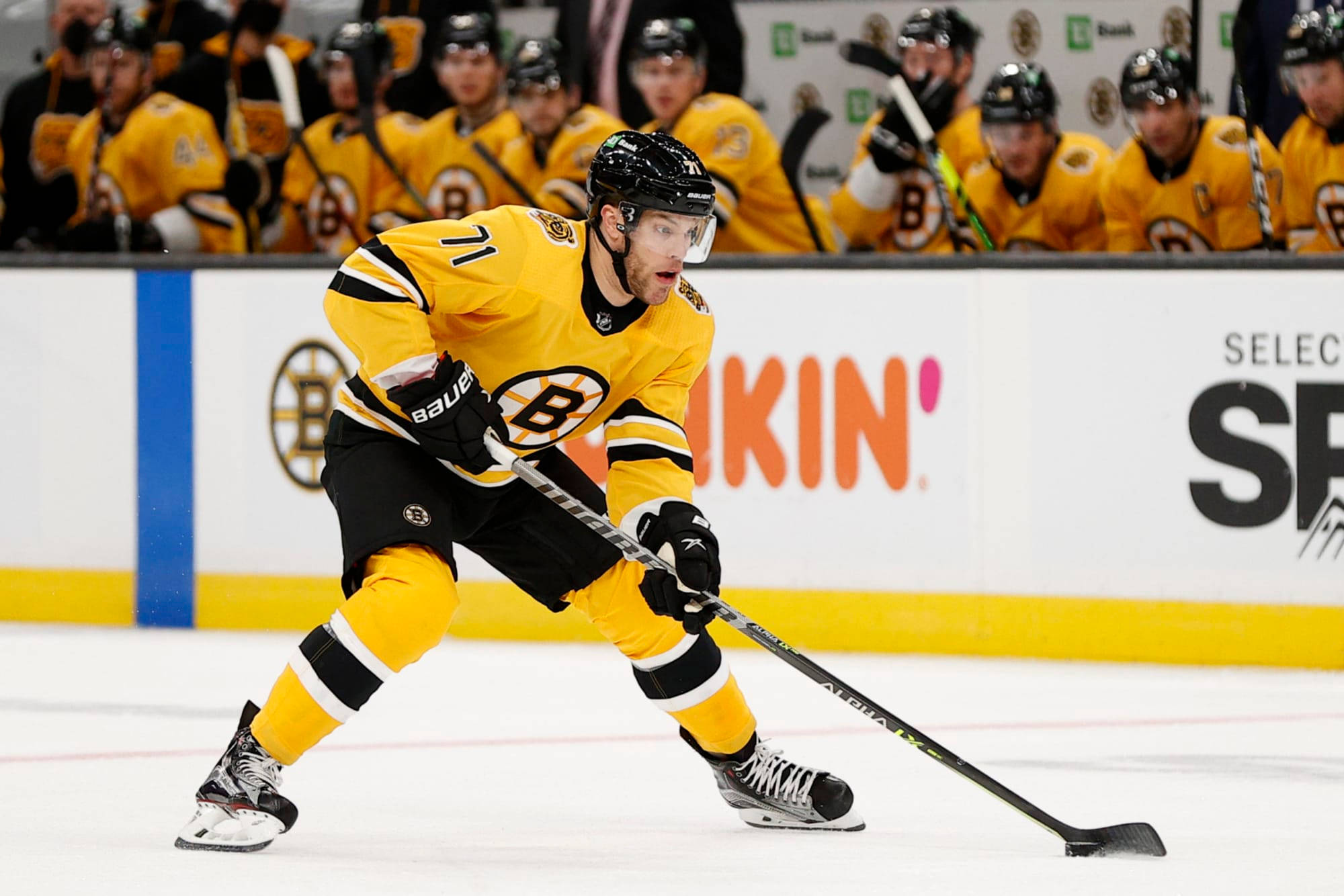 hockey 桌布 壁紙 — 一名身穿黃黑制服的冰球運動員在冰上激烈溜冰，隊友在長凳上觀看。