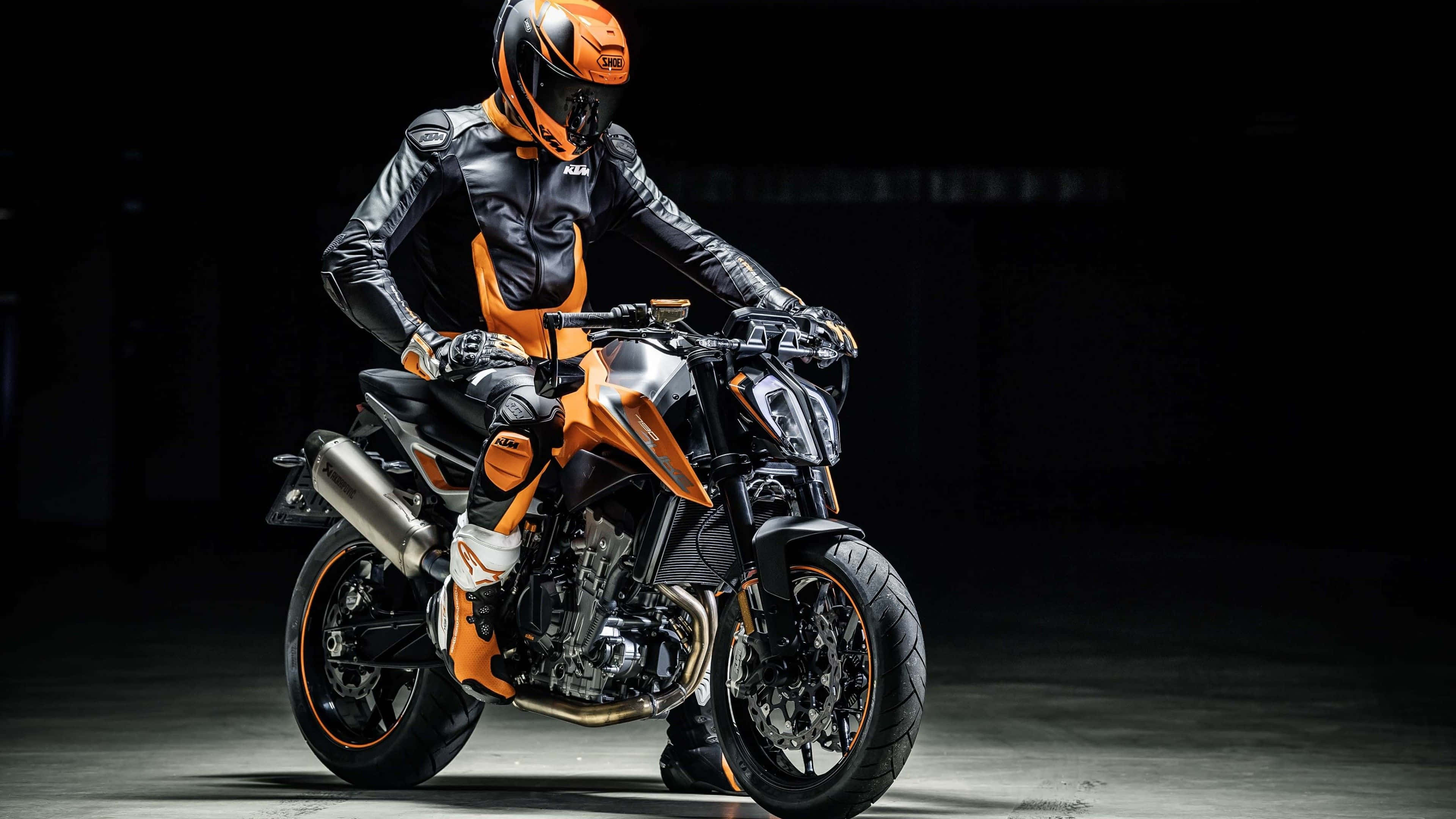 Ktm Bike 桌布 壁紙 — 一名身穿黑橙色裝備的騎士，在戲劇性的工作室燈光下，坐在流線型的KTM摩托車上，蓄勢待發。