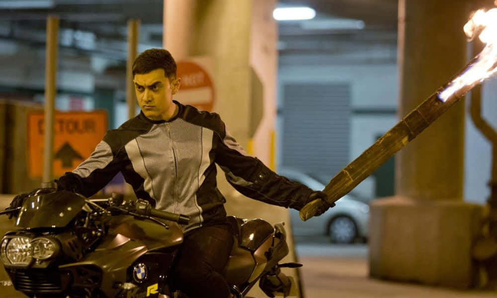Aamir Khan 桌布 壁紙 — 一名身穿黑灰色賽車服的男子坐在一輛時尚的摩托車上，在光線昏暗的地下停車場中手持燃燒的火把。