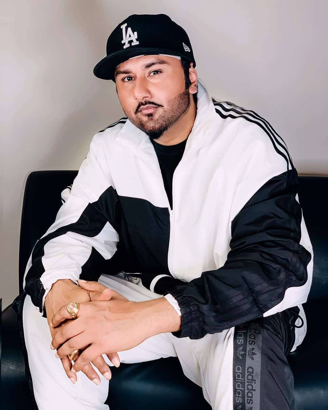 Celebrity 桌布 壁紙 — 一名身穿黑白Adidas運動套裝和LA帽子的男子自信地坐在黑色椅子上，雙手緊握。