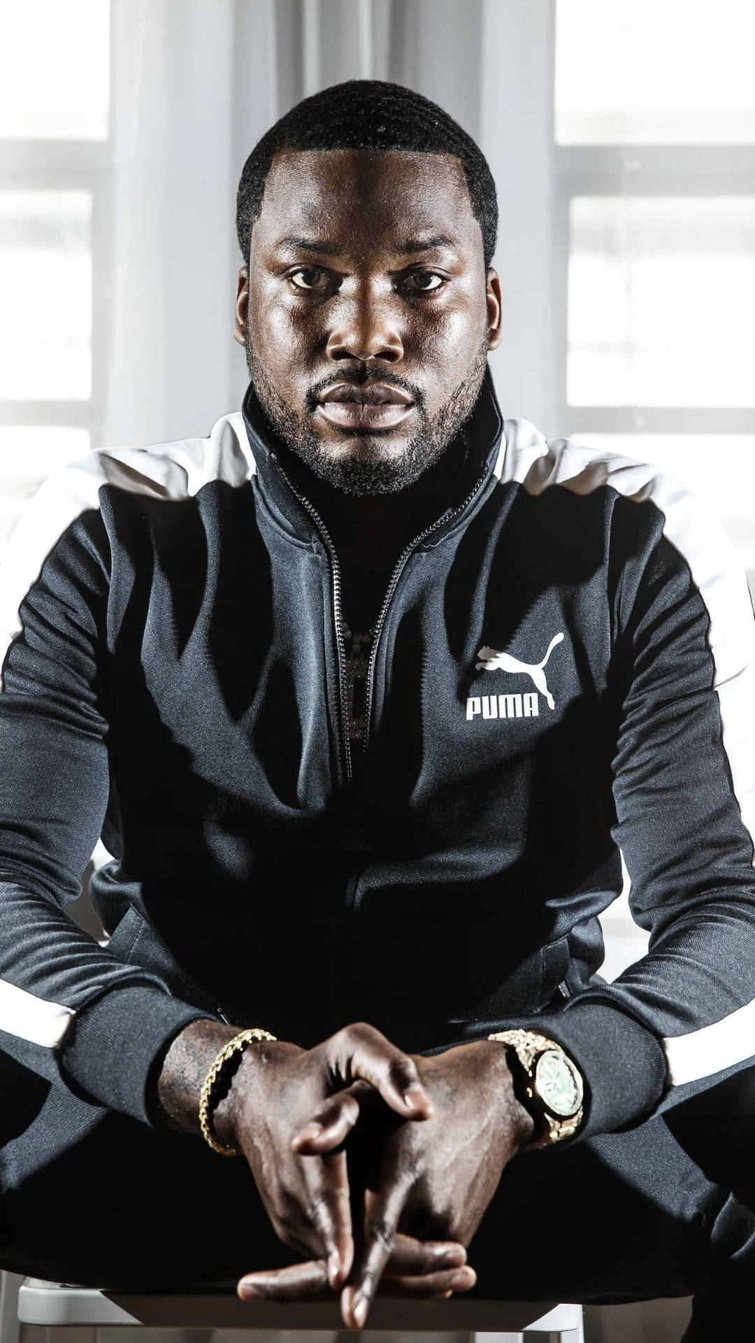 Mill 桌布 壁紙 — 一名身穿黑白Puma運動服的男子自信地坐在明亮的窗戶背景前，雙手緊握。