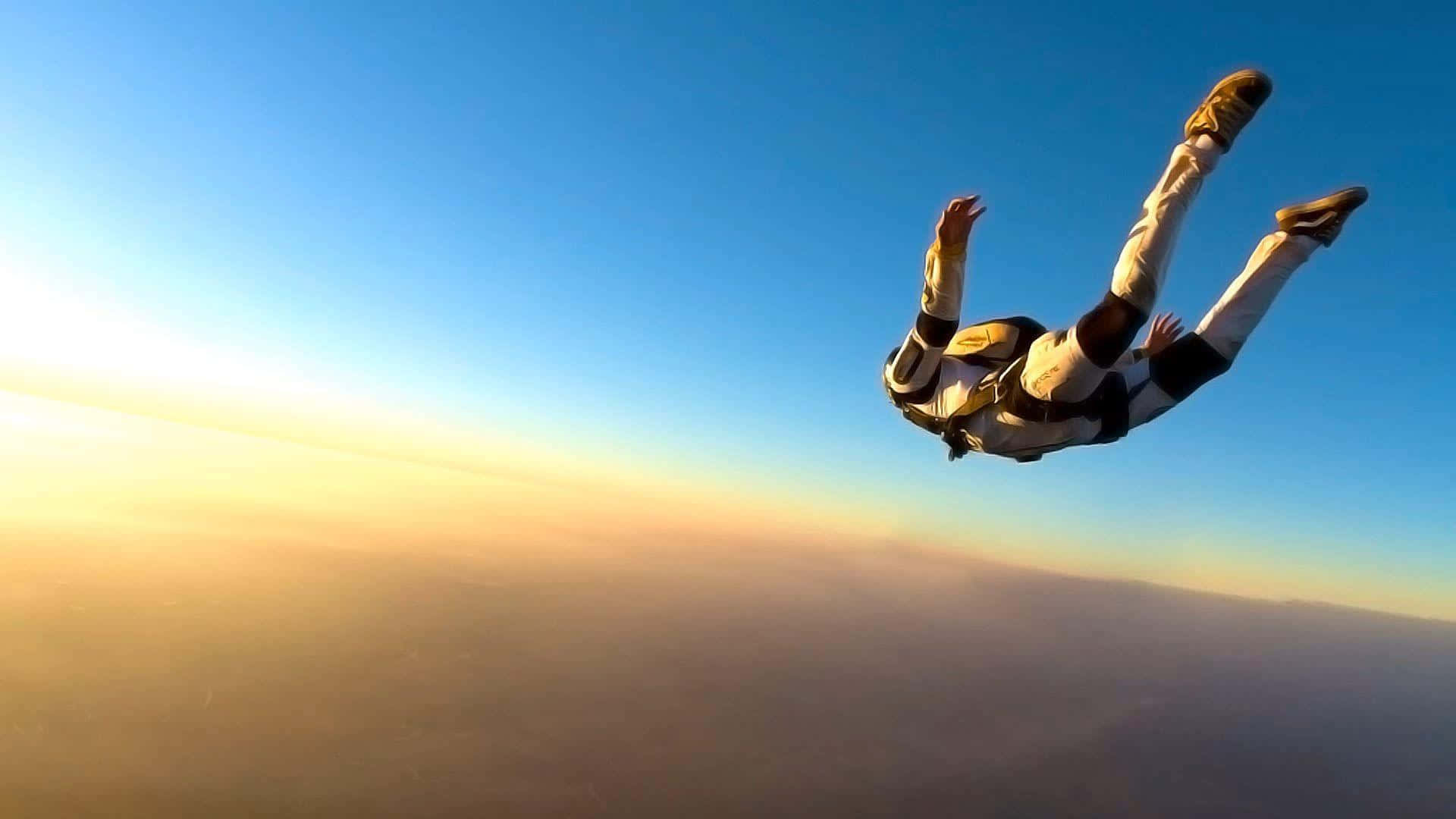 Skydiving 桌布 壁紙 — 一名身穿黑白套裝的跳傘運動員在日落時分，穿過晴朗的藍天，在金色雲層下方自由墜落。