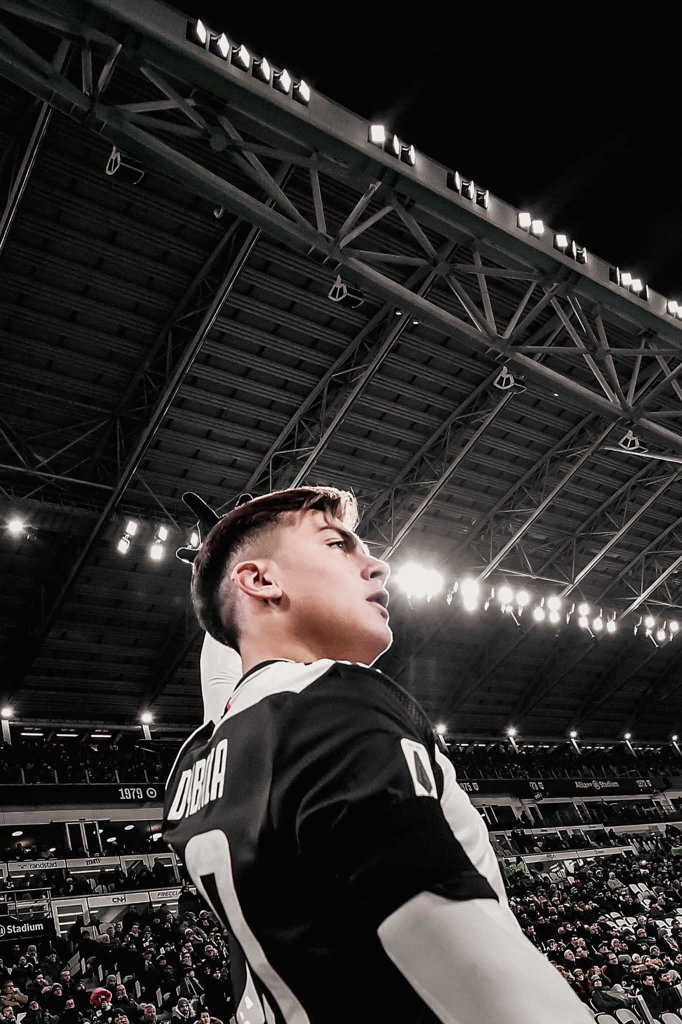 Football Players 桌布 壁紙 — 一名身穿黑白球衣的足球員在明亮的燈光下站在球場上，身後有觀眾。
