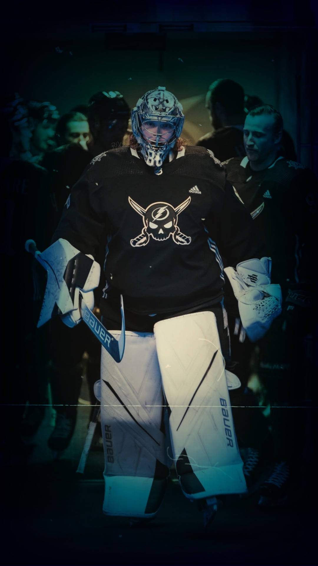 hockey 桌布 壁紙 — 一名身穿黑白裝備的冰球守門員在昏暗的場館燈光下擺好姿勢，背景中的隊友模糊不清。
