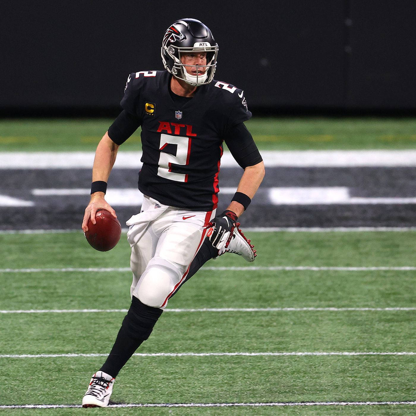 Matt Ryan 桌布 壁紙 — 一名身穿黑紅球衣的美式足球四分衛在球場燈光下，手持橄欖球衝過綠色球場。