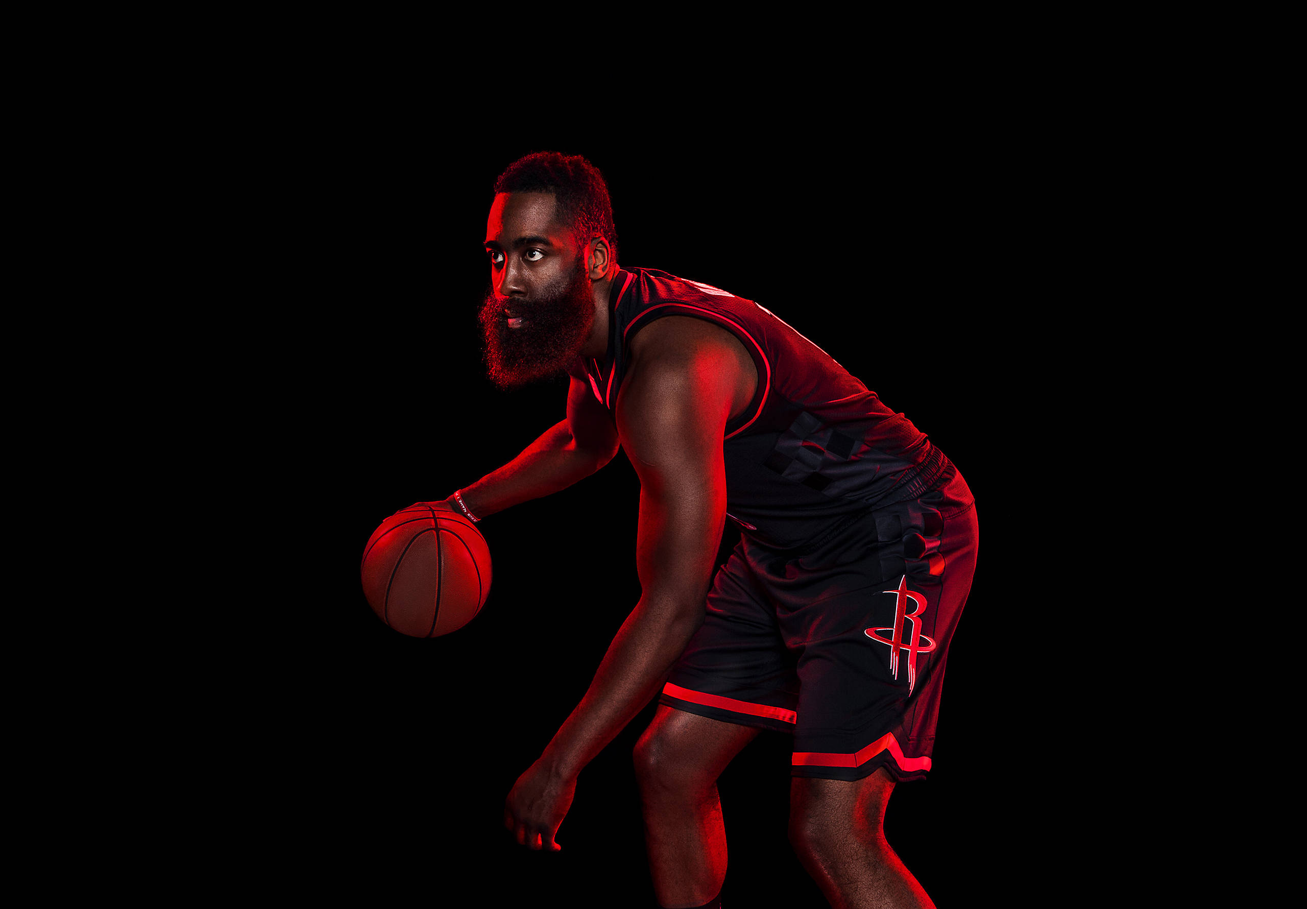James Harden 桌布 壁紙 — 一名身穿黑紅色球衣的籃球運動員，在戲劇性的紅色燈光照射下，對著漆黑的背景，蹲下身子，緊緊地拿著球。