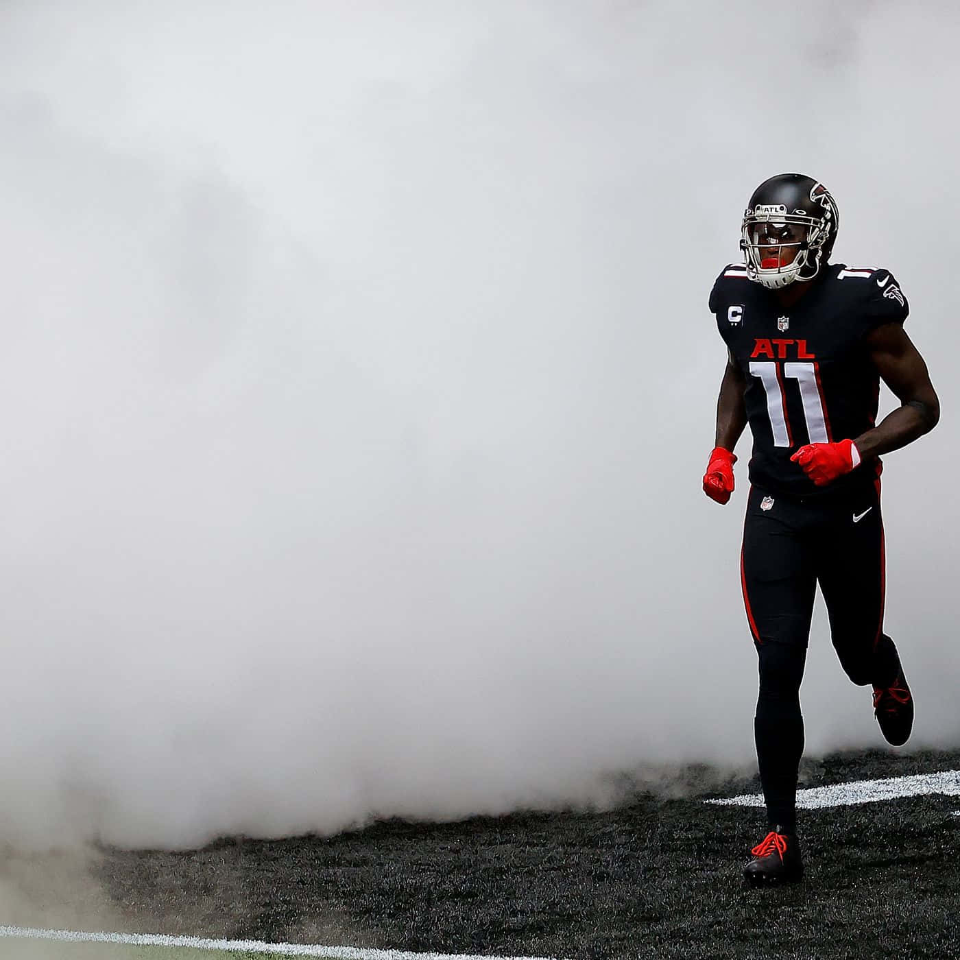 Julio Jones 桌布 壁紙 — 一名身穿黑紅色球衣的足球員在帶有白色線條的球場上穿過濃煙奔跑。