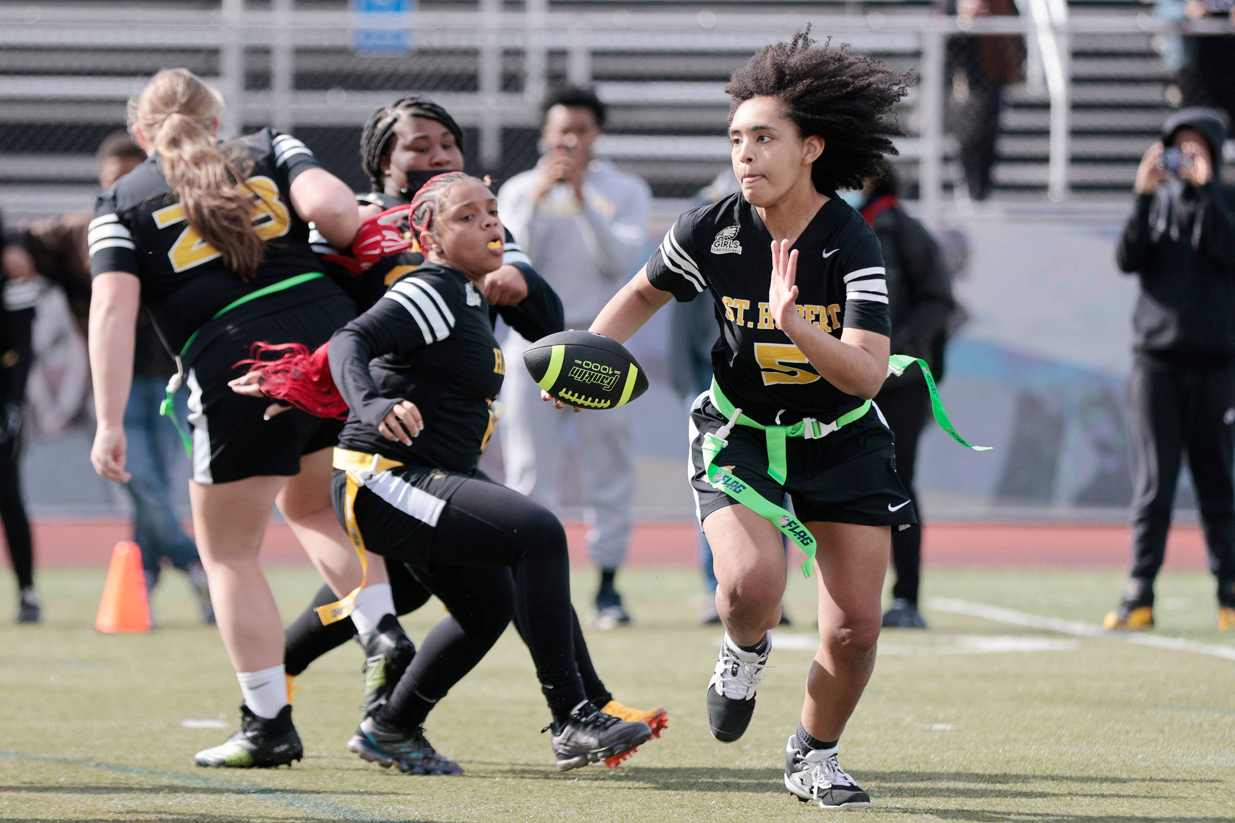 Football Players 桌布 壁紙 — 一名身穿黑綠色制服的女旗足球員在陽光明媚的球場上持球衝刺，對手在後面追趕。