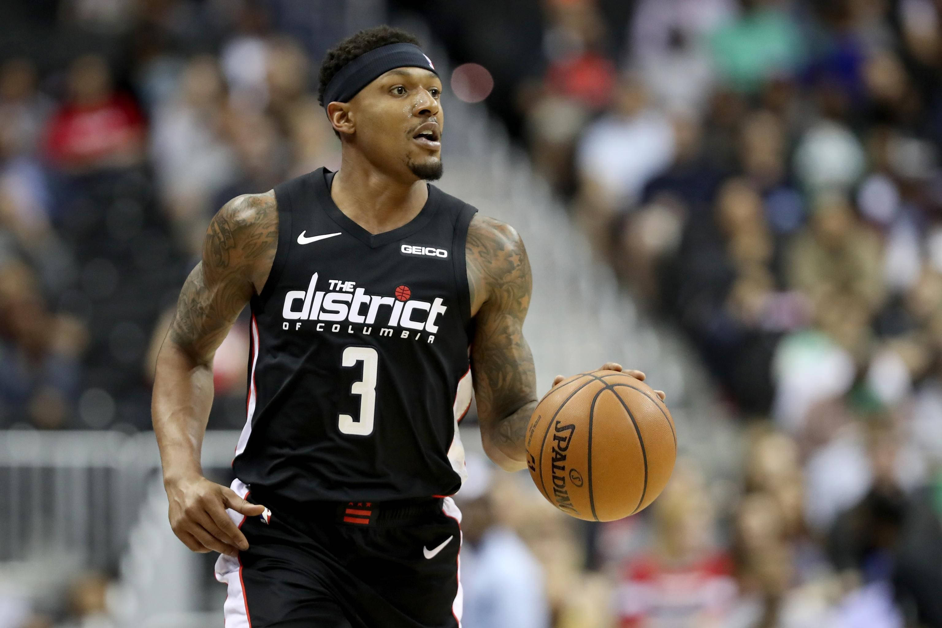 Bradley Beal 桌布 壁紙 — 一名身穿黑色「The District of Columbia」球衣的籃球運動員，在模糊的人群背景下，於激烈的比賽中運著Spalding球。