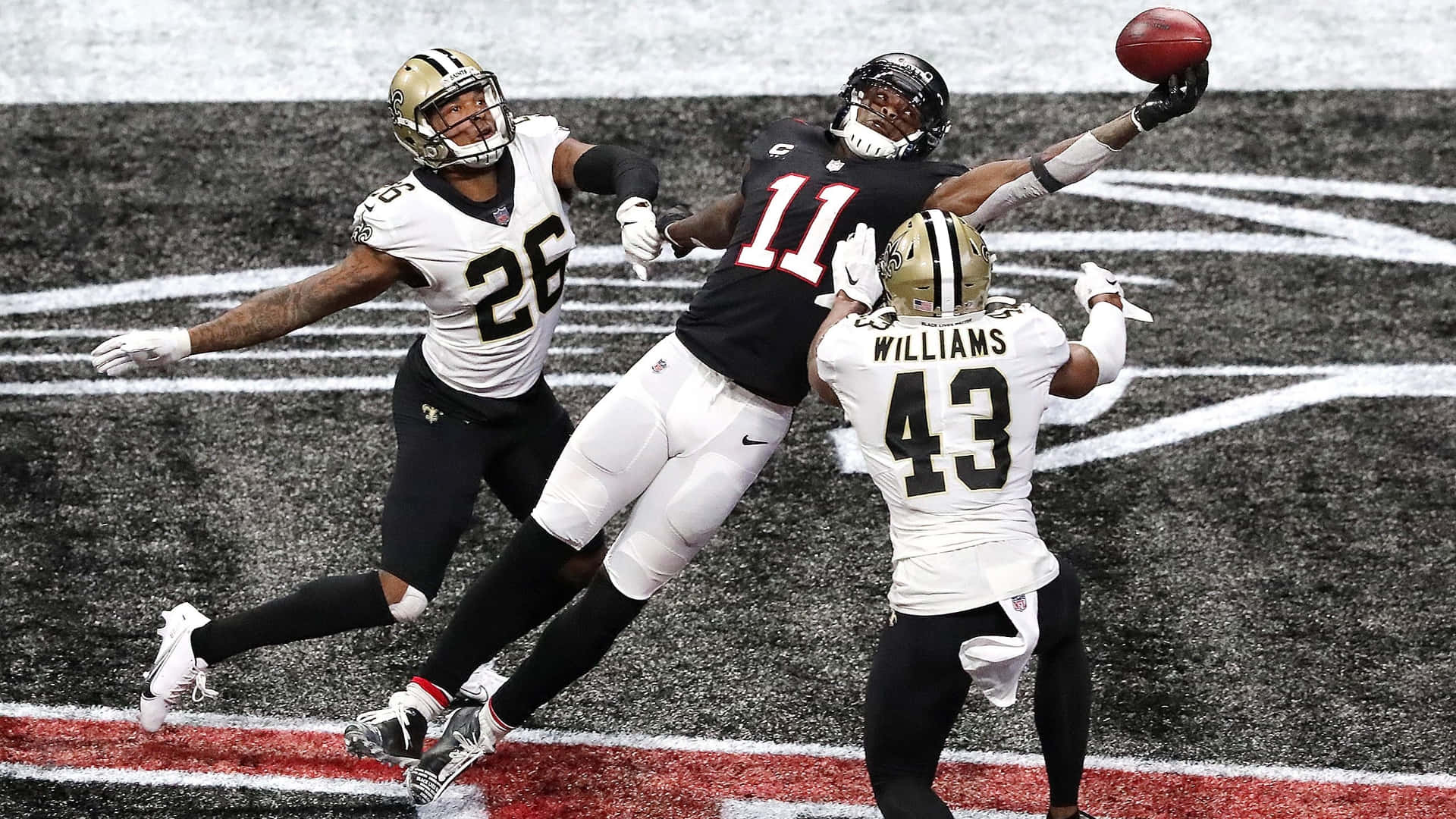 Julio Jones 桌布 壁紙 — 一名身穿黑色11號球衣的足球員跳起接球，兩名白色球衣的防守球員在場上攔截他。