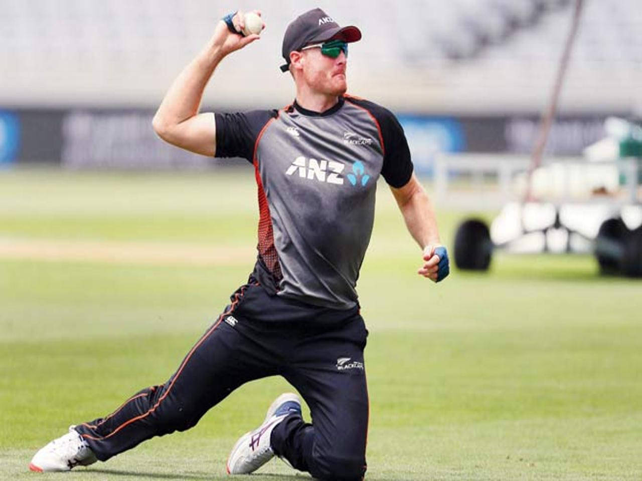 martin guptill 桌布 壁紙 — 一名身穿黑色ANZ制服的板球運動員在明亮的日光下，在綠色場地上專注地投球。