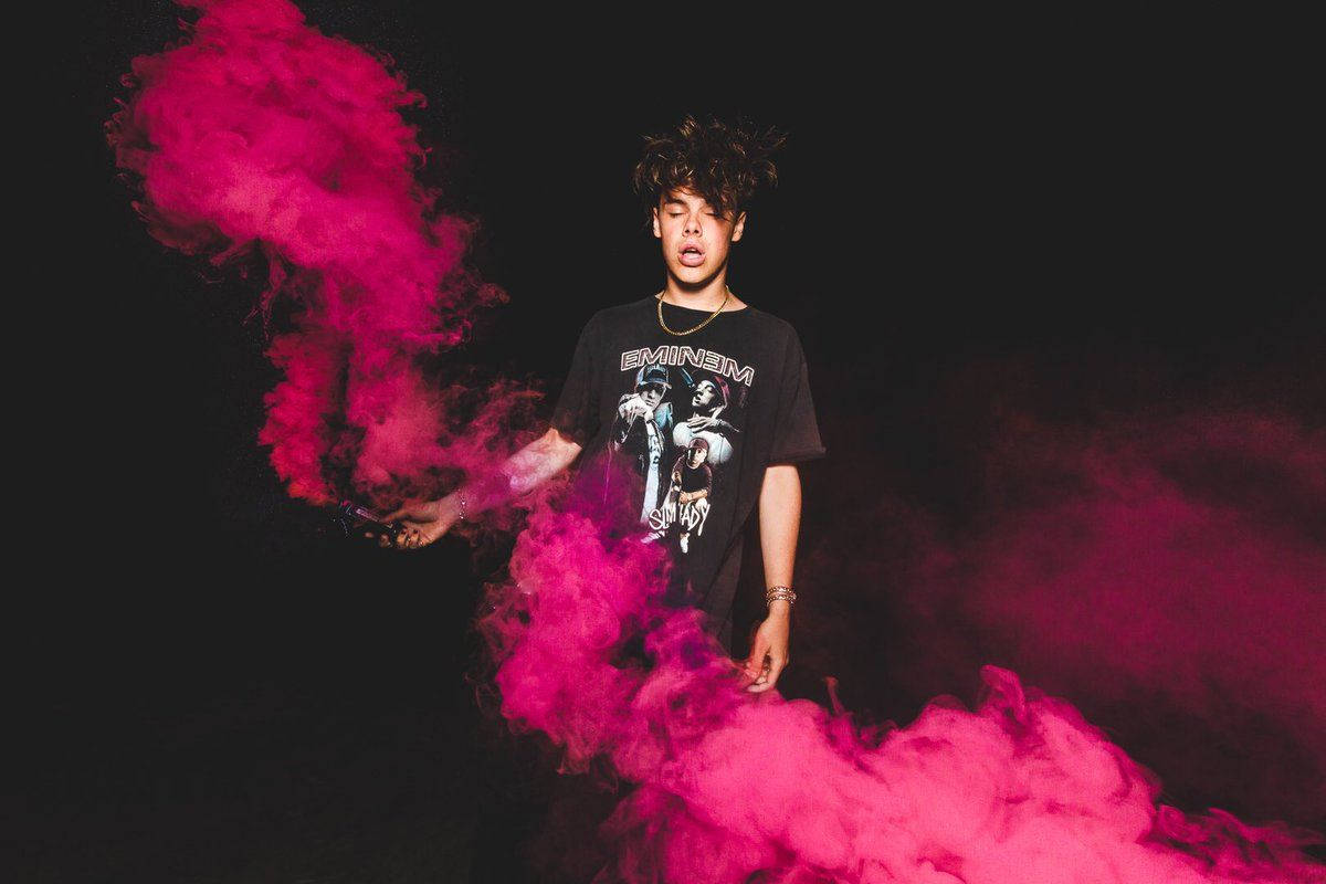 Pink And Black 桌布 壁紙 — 一名身穿黑色Eminem T恤的年輕男子站在黑暗背景中，周圍環繞著旋轉的鮮豔粉紅色煙霧。