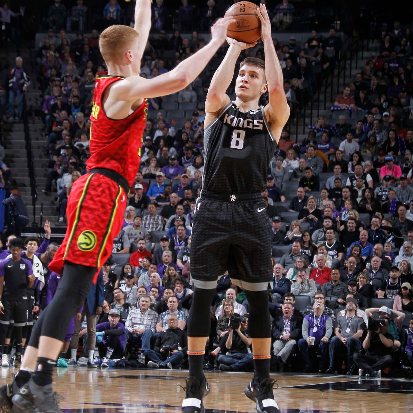 NBA 桌布 壁紙 — 一名身穿黑色Kings球衣的籃球運動員跳投，而一名身穿紅色球衣的防守球員在擠滿人的場館中跳起封阻他。