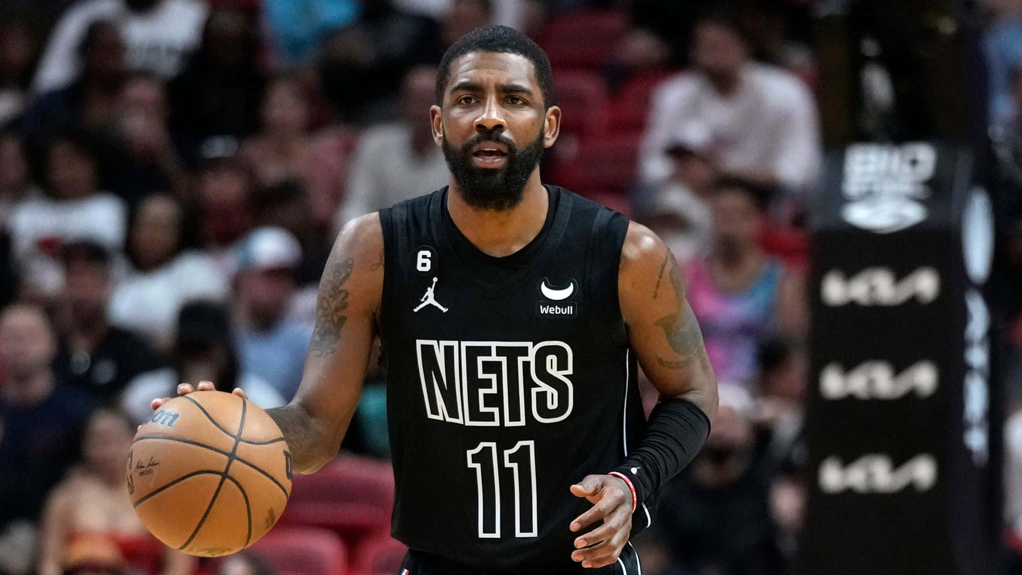 Kyrie Irving Nets 桌布 壁紙 — 一名身穿黑色Nets球衣的籃球運動員在比賽中運球，背景是模糊的人群。