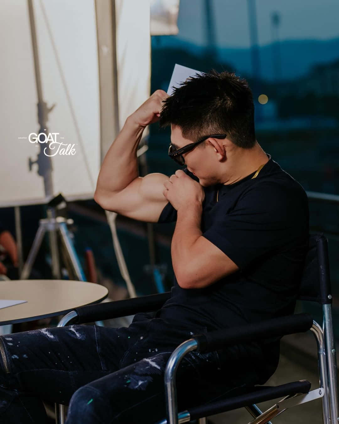 Fitness 桌布 壁紙 — 一名身穿黑色T恤的男子坐在導演椅上，室內可見攝影棚設備，他正彎曲肱二頭肌。