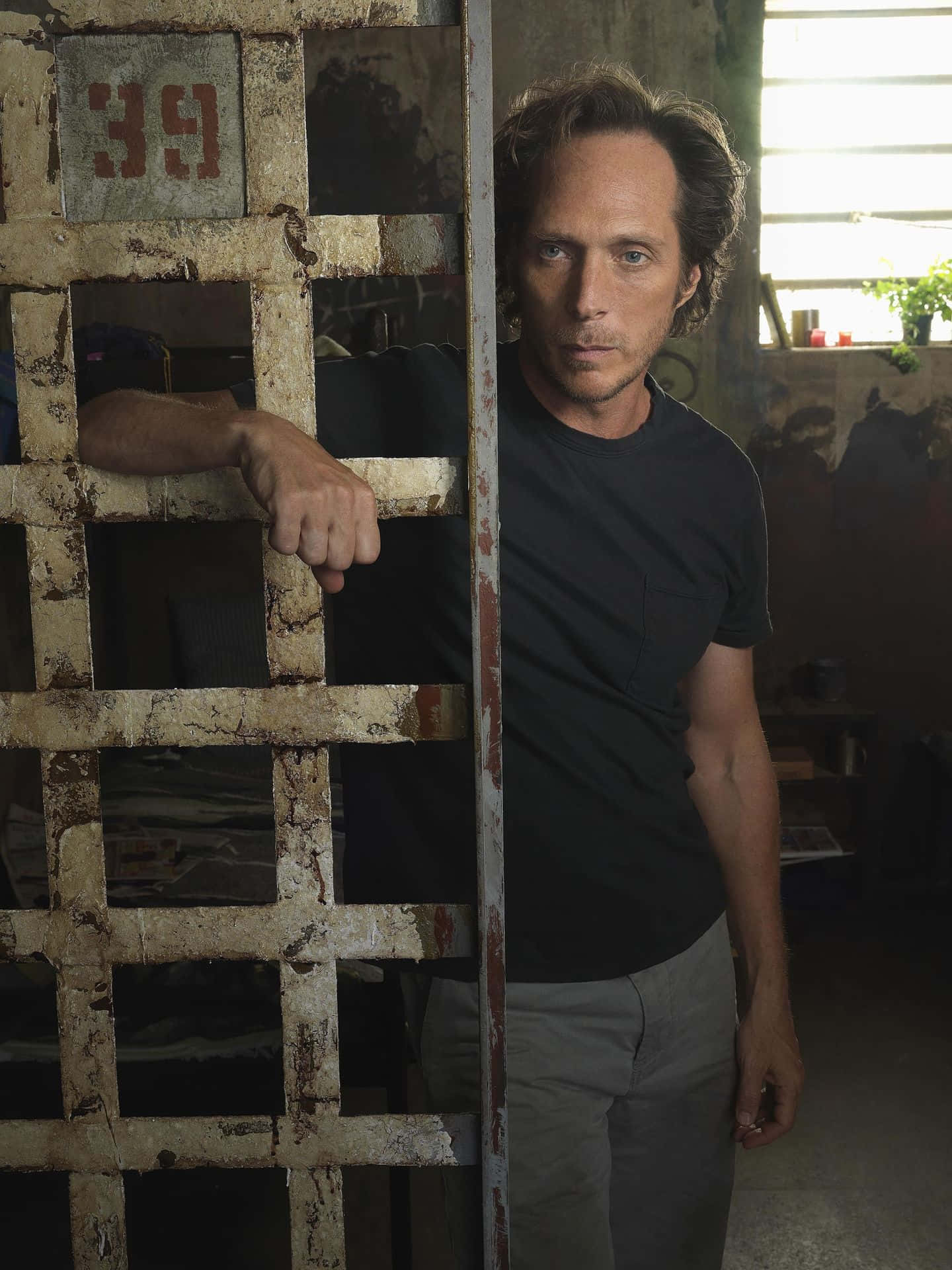 William Fichtner 桌布 壁紙 — 一名身穿黑色T恤的男子站在一扇標有69的鏽蝕金屬監獄牢門後面，神情嚴肅地抓著鐵欄杆。