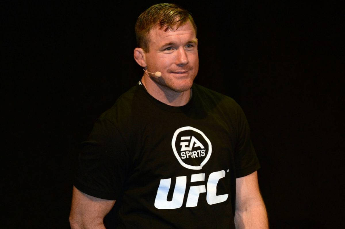UFC 桌布 壁紙 — 一名身穿黑色UFC T恤的男子在深色背景下戴著耳機微笑。
