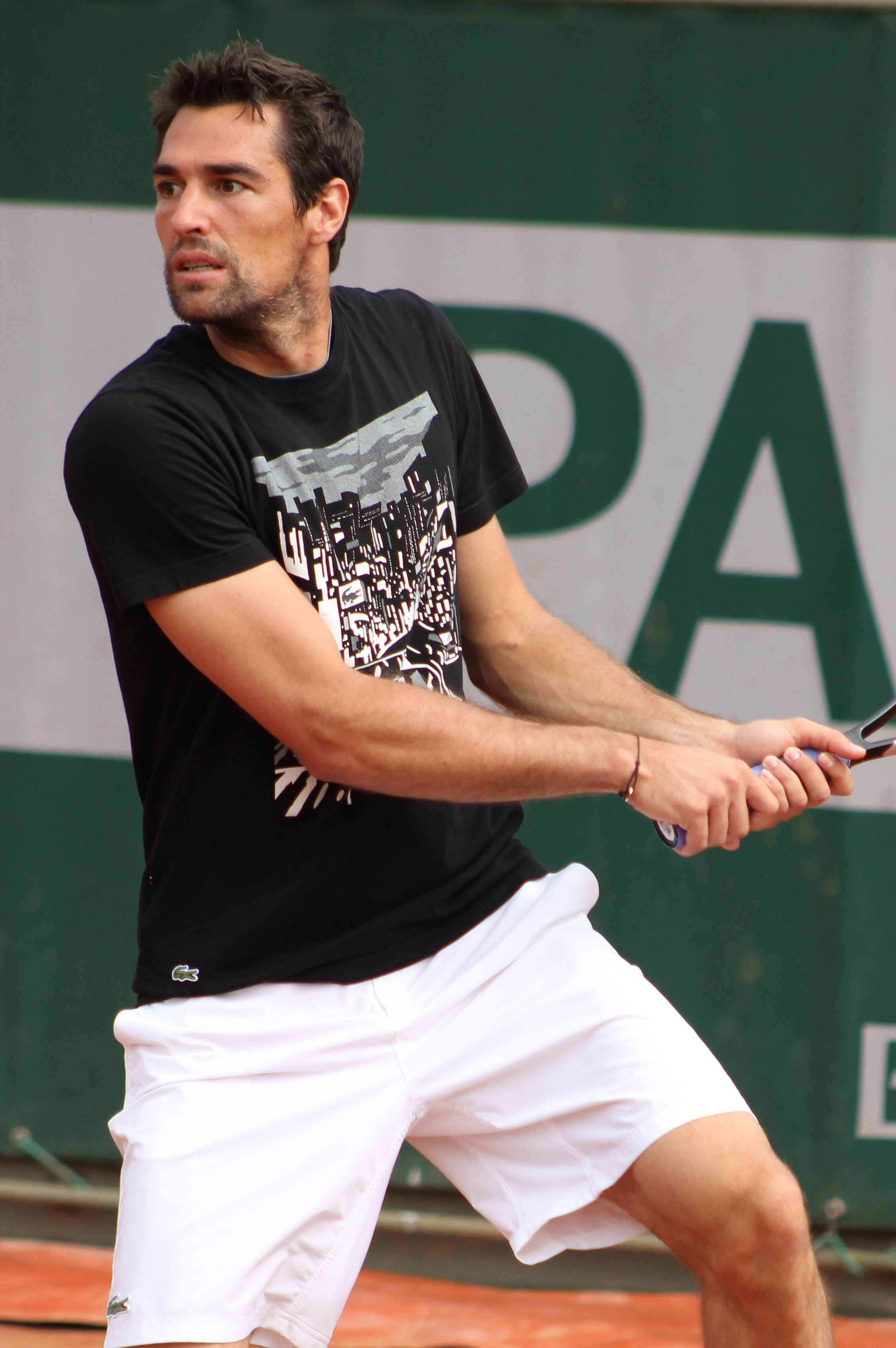 Tennis 桌布 壁紙 — 一名身穿黑色上衣和白色短褲的男性網球選手在紅土球場上專注地揮拍。