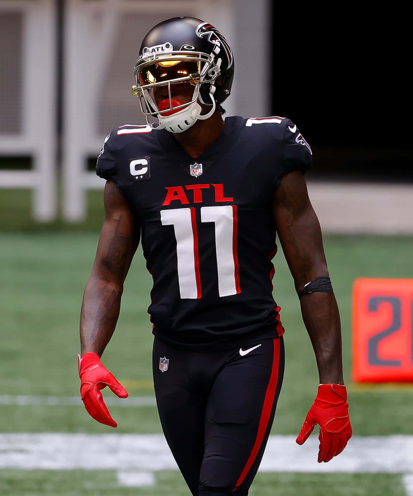 Julio Jones 桌布 壁紙 — 一名身穿黑色亞特蘭大獵鷹隊制服、戴紅色手套的足球員在綠色球場上行走。