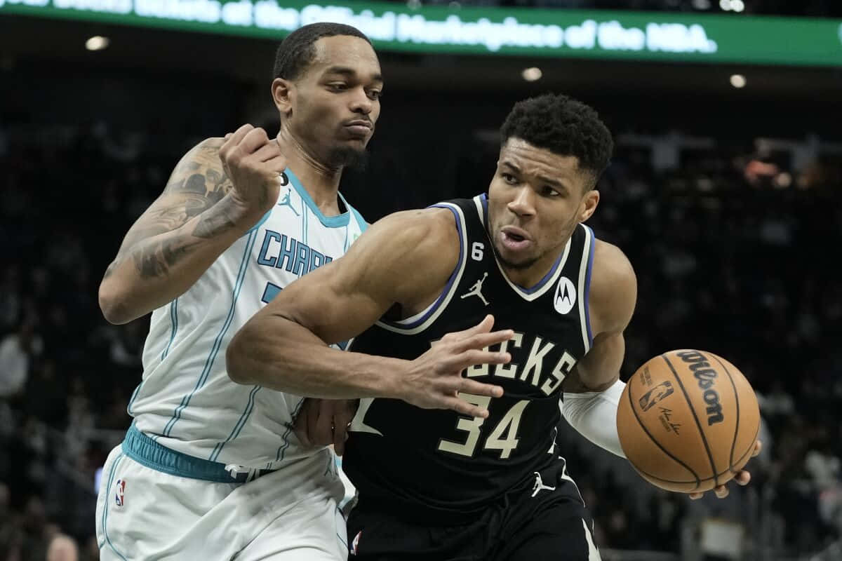 Bucks 桌布 壁紙 — 一名身穿黑色公鹿隊球衣的籃球運動員在激烈的NBA比賽中帶球越過一名身穿白色黃蜂隊球衣的防守球員。