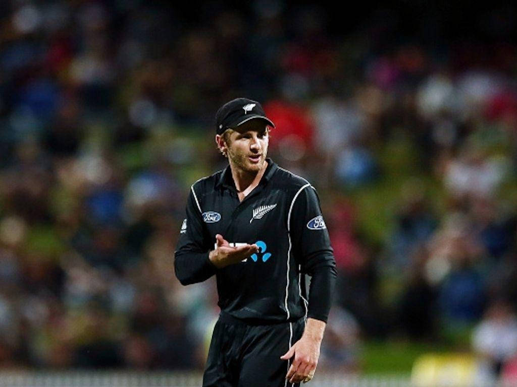 kane williamson 桌布 壁紙 — 一名身穿黑色制服的新西蘭板球運動員在夜間比賽中，在球場燈光下做出手勢，背景是模糊的人群。