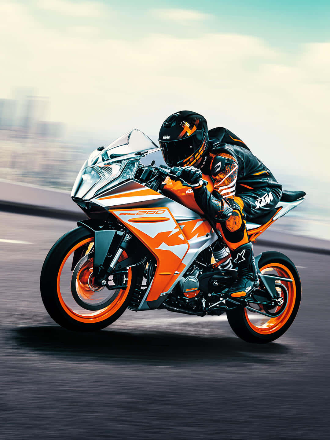 機車 桌布 壁紙 — 一名身穿黑色和橙色裝備的騎士在KTM RC 200摩托車上傾斜入彎，城市道路上帶有動態模糊效果。