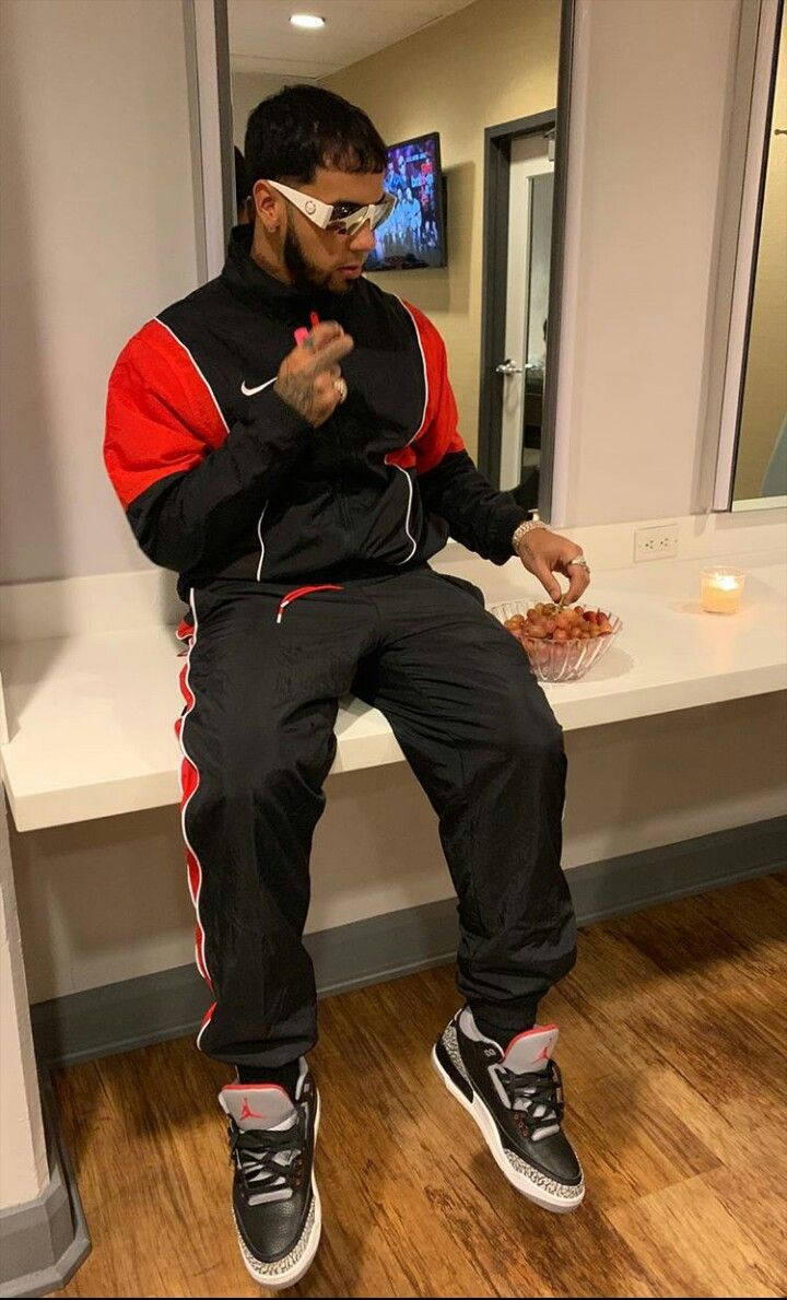 aa 桌布 壁紙 — 一名身穿黑色和紅色運動服的男子隨意地坐在白色櫃檯上，戴著白色太陽眼鏡吃零食。