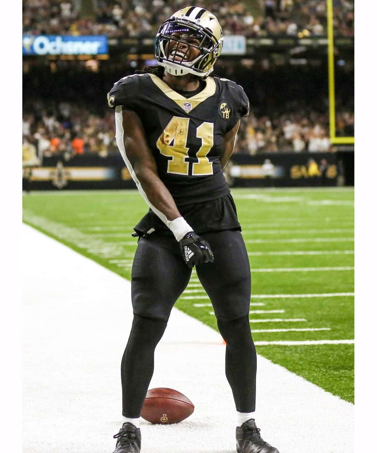 Alvin Kamara 桌布 壁紙 — 一名身穿黑色和金色球衣的41號足球運動員在燈光球場上慶祝，腳邊有球。