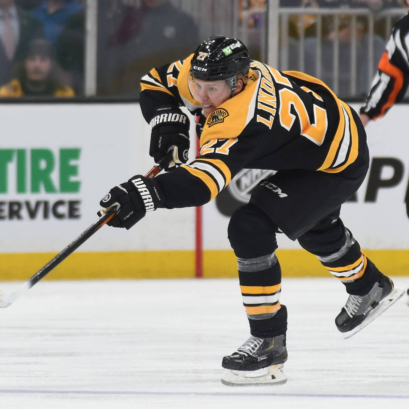 hockey 桌布 壁紙 — 一名身穿黑色和金色球衣的冰球運動員在比賽中，在人群背景的冰上激烈地向前傾身。