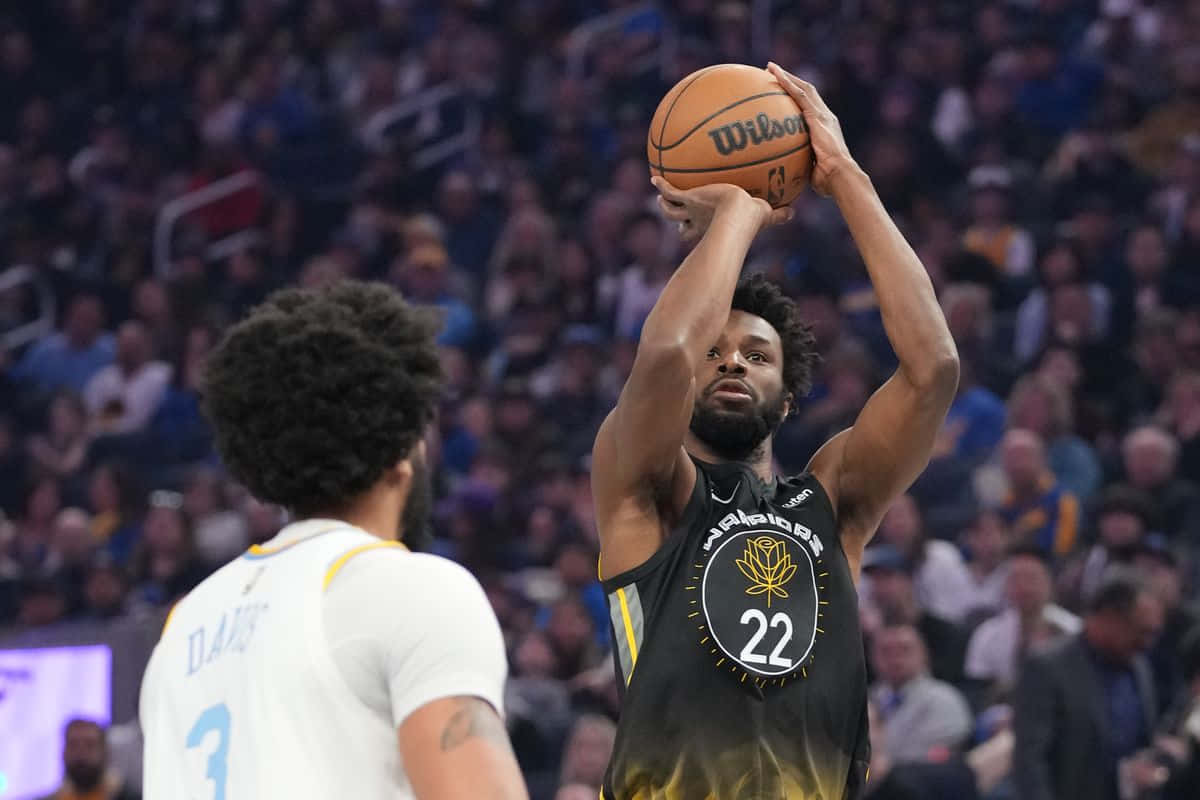 Andrew Wiggins 桌布 壁紙 — 一名身穿黑色和金色球衣的籃球運動員在比賽中準備投籃，背景是模糊的人群。