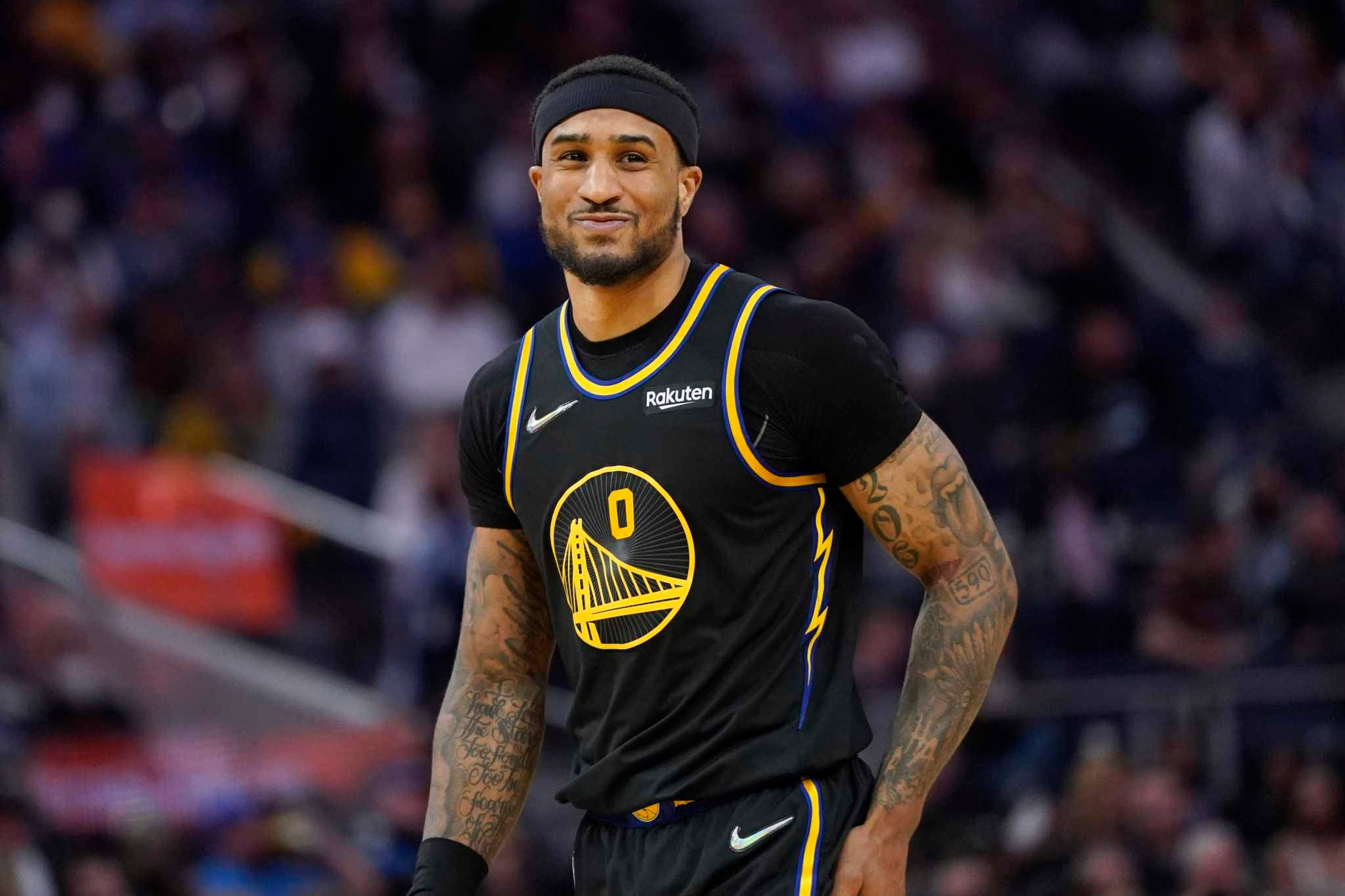NBA 桌布 壁紙 — 一名身穿黑色和金色球衣的籃球運動員在燈光球場上自信微笑，身後是模糊的觀眾。