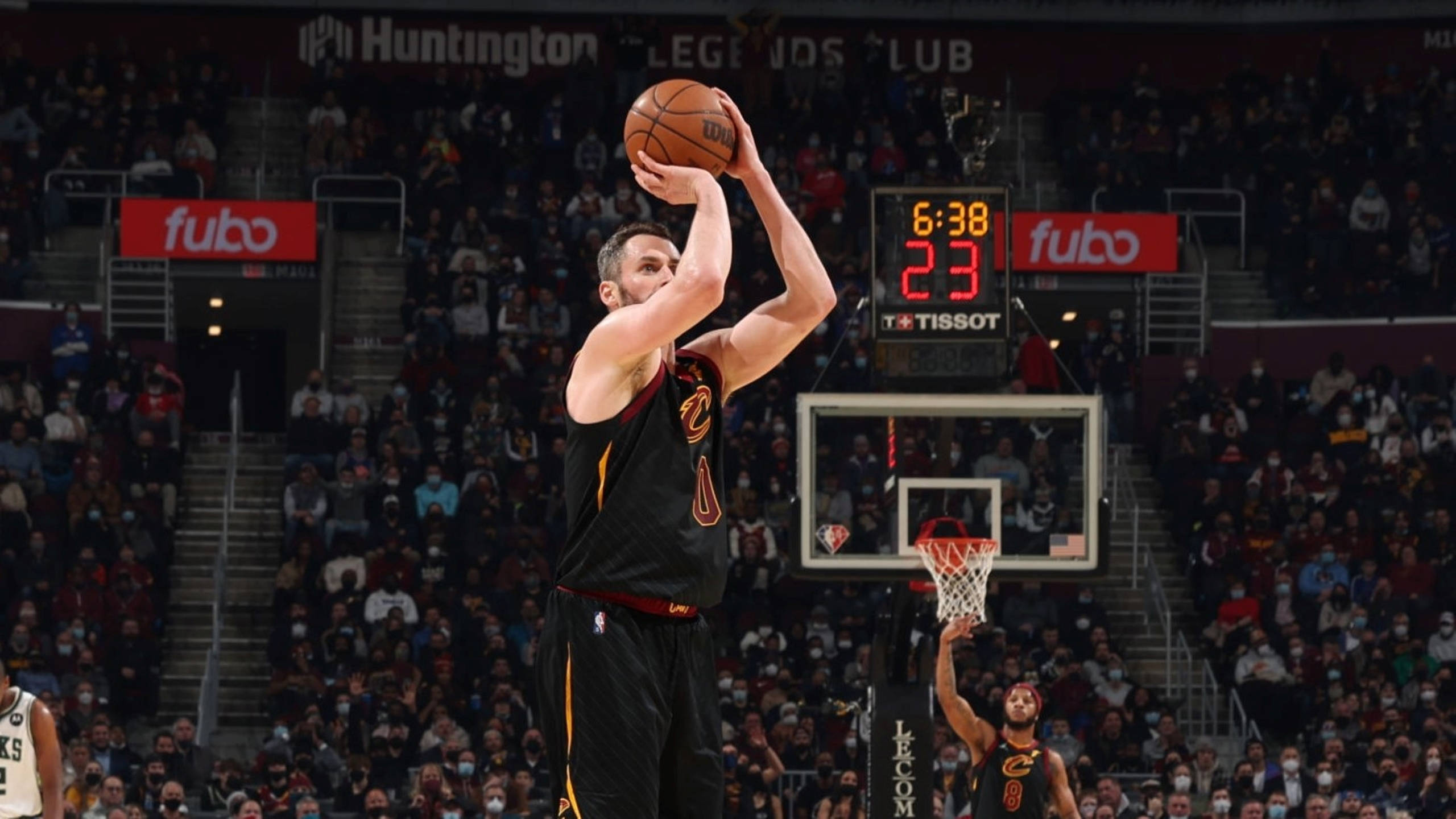 Kevin Love 桌布 壁紙 — 一名身穿黑色和金色球衣的籃球運動員在比賽中跳投，背景是擠滿觀眾的體育館和記分板。