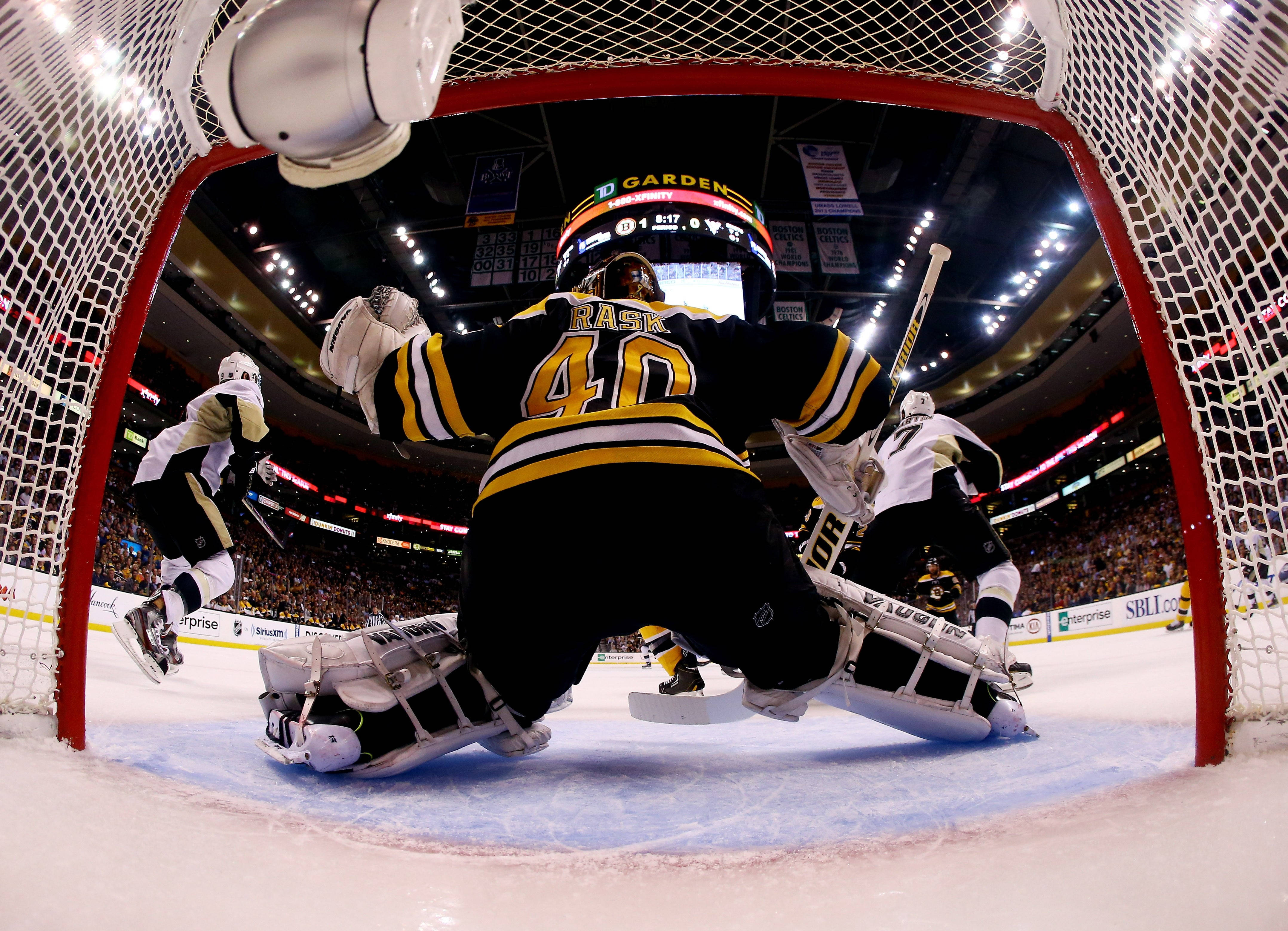 hockey 桌布 壁紙 — 一名身穿黑色和金色裝備的冰球守門員在TD Garden的激烈比賽中從球網後方做出戲劇性的撲救。