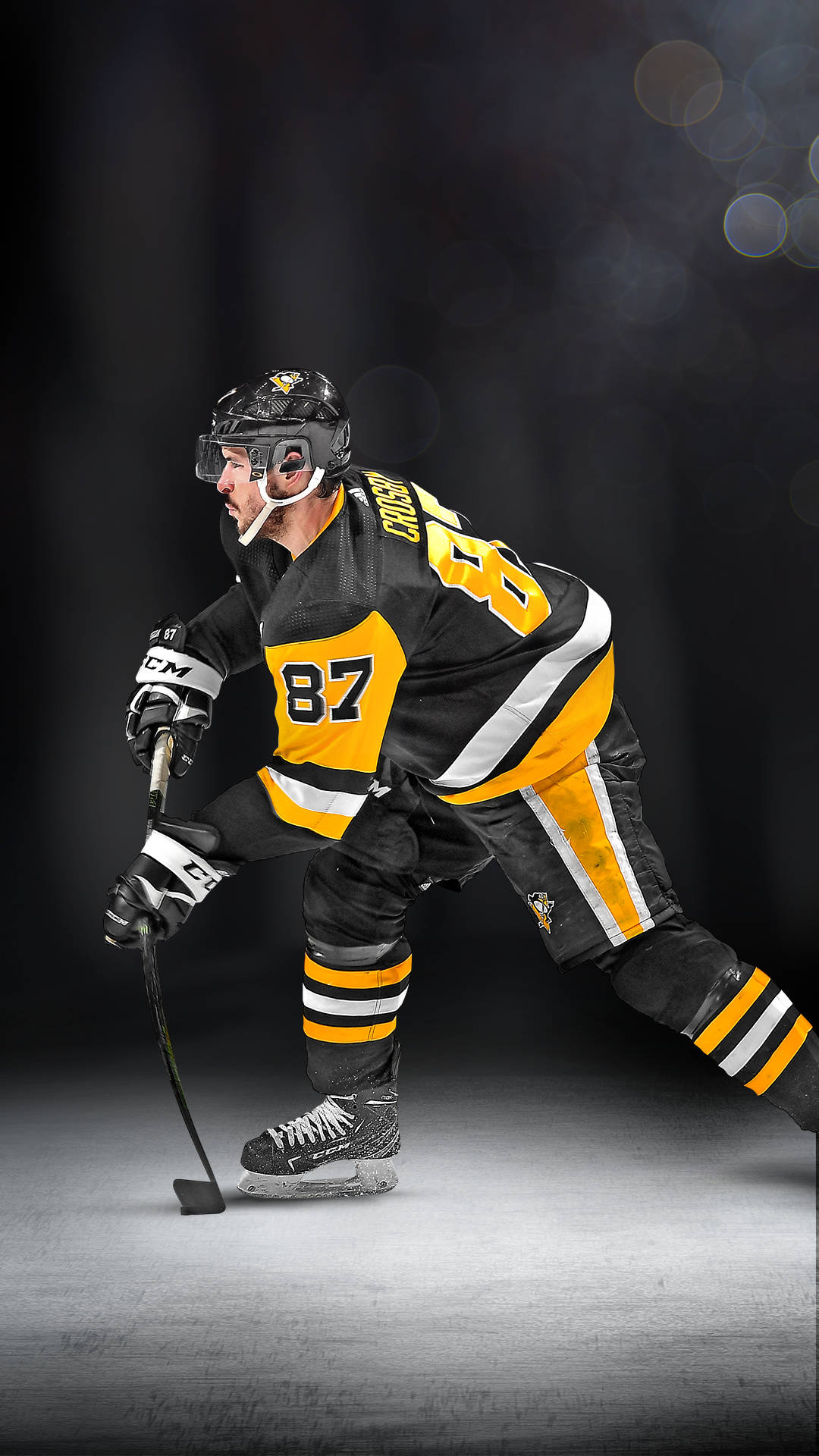 penguins 桌布 壁紙 — 一名身穿黑色和黃色裝備的曲棍球運動員在冰上蹲低，手持球桿，背景是帶有散景燈光的黑暗工作室。