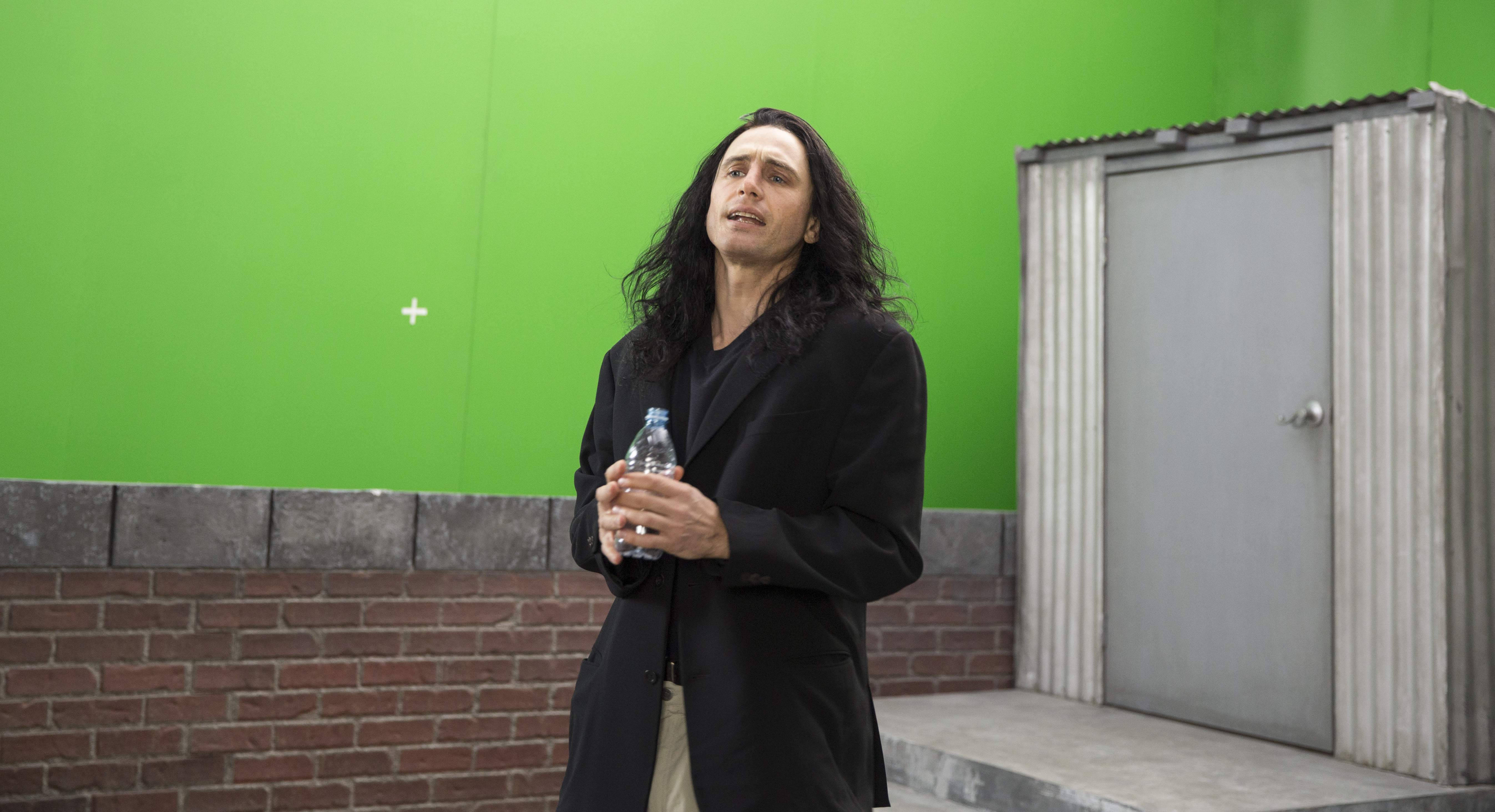 Celebrity 桌布 壁紙 — 一名身穿黑色外套、留著深色長髮的男子，在鮮綠色螢幕和磚牆前拿著一個水瓶。