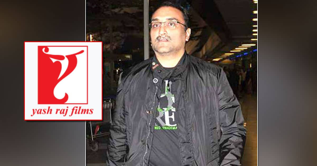 電影動圖 桌布 壁紙 — 一名身穿黑色外套和戴眼鏡的男子站在Yash Raj Films標誌旁邊，室內環境背景燈光模糊。