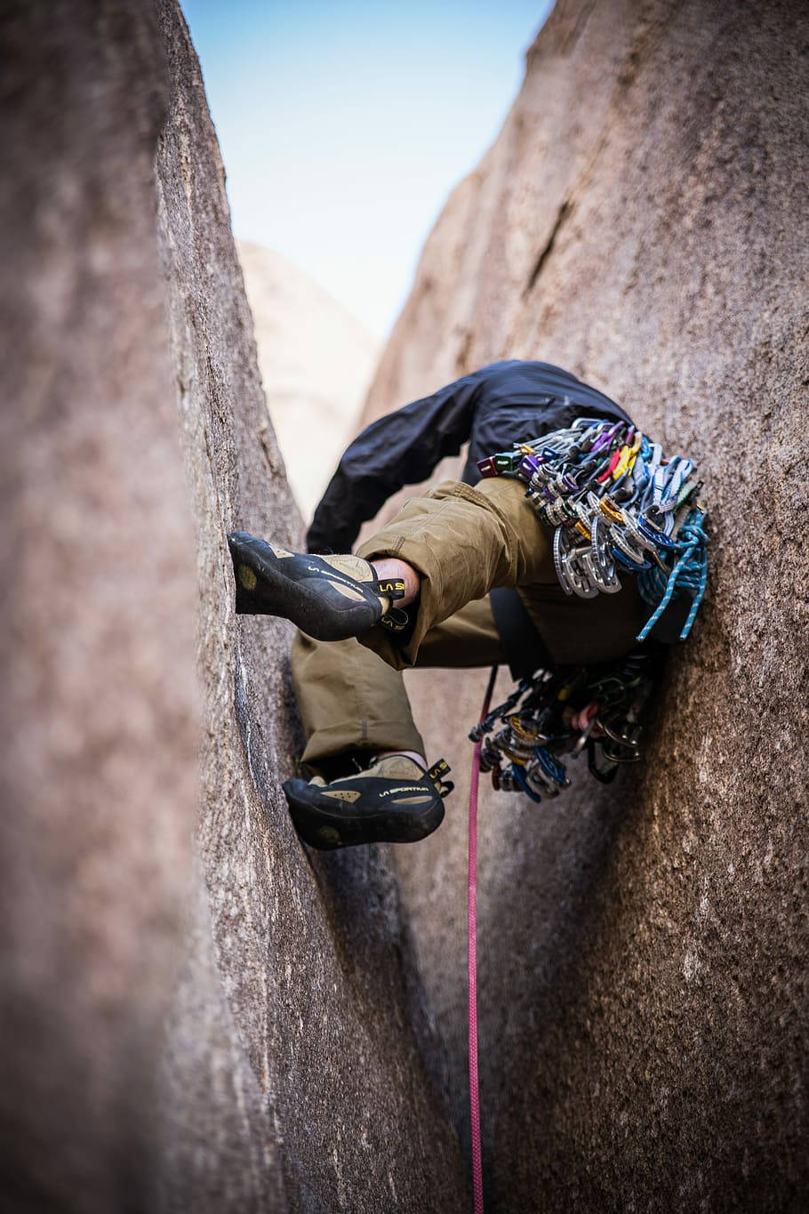 Rock Climbing 桌布 壁紙 — 一名身穿黑色外套和棕色褲子的攀岩者，帶著裝備和粉紅色繩索，攀登狹窄的岩石裂縫。