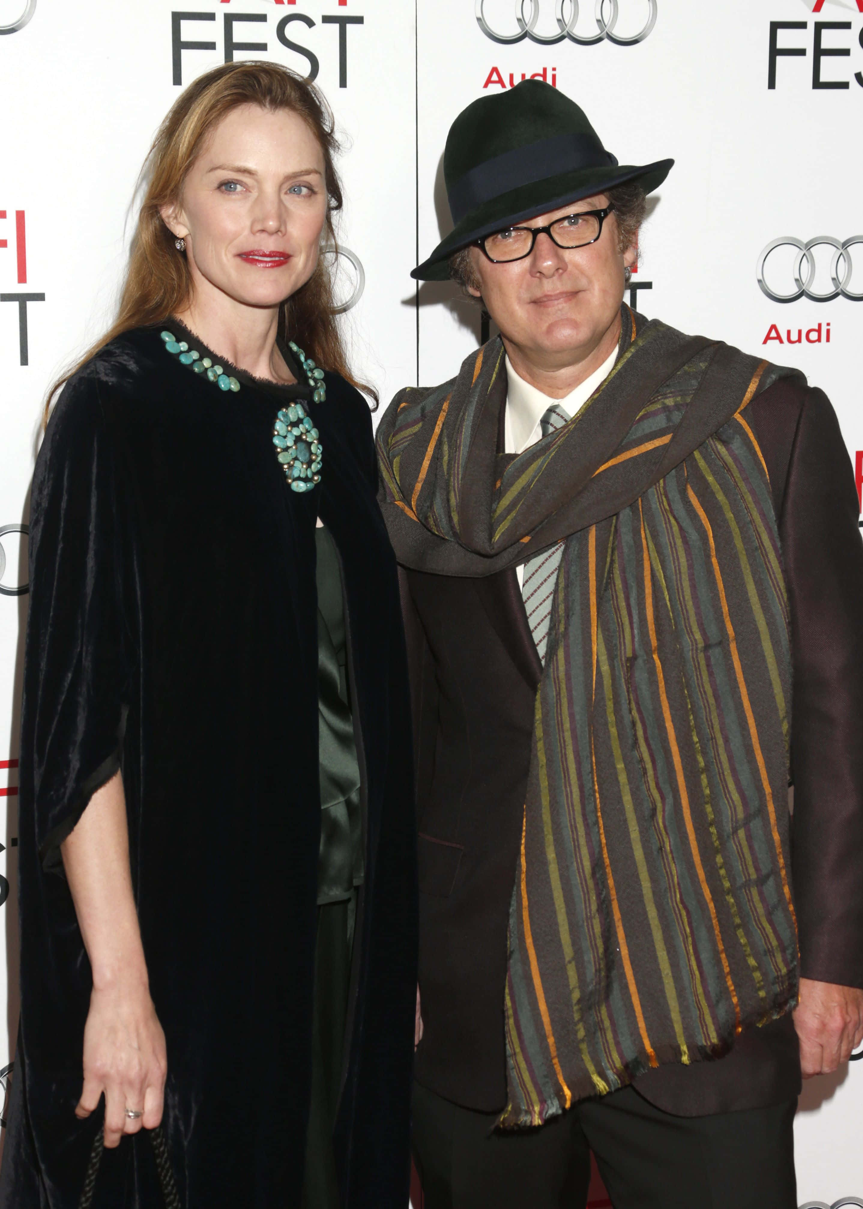 james spader 桌布 壁紙 — 一名身穿黑色天鵝絨斗篷、佩戴綠松石珠寶的女性，與一名戴著軟呢帽和條紋圍巾的男性在電影節活動中並肩而立。
