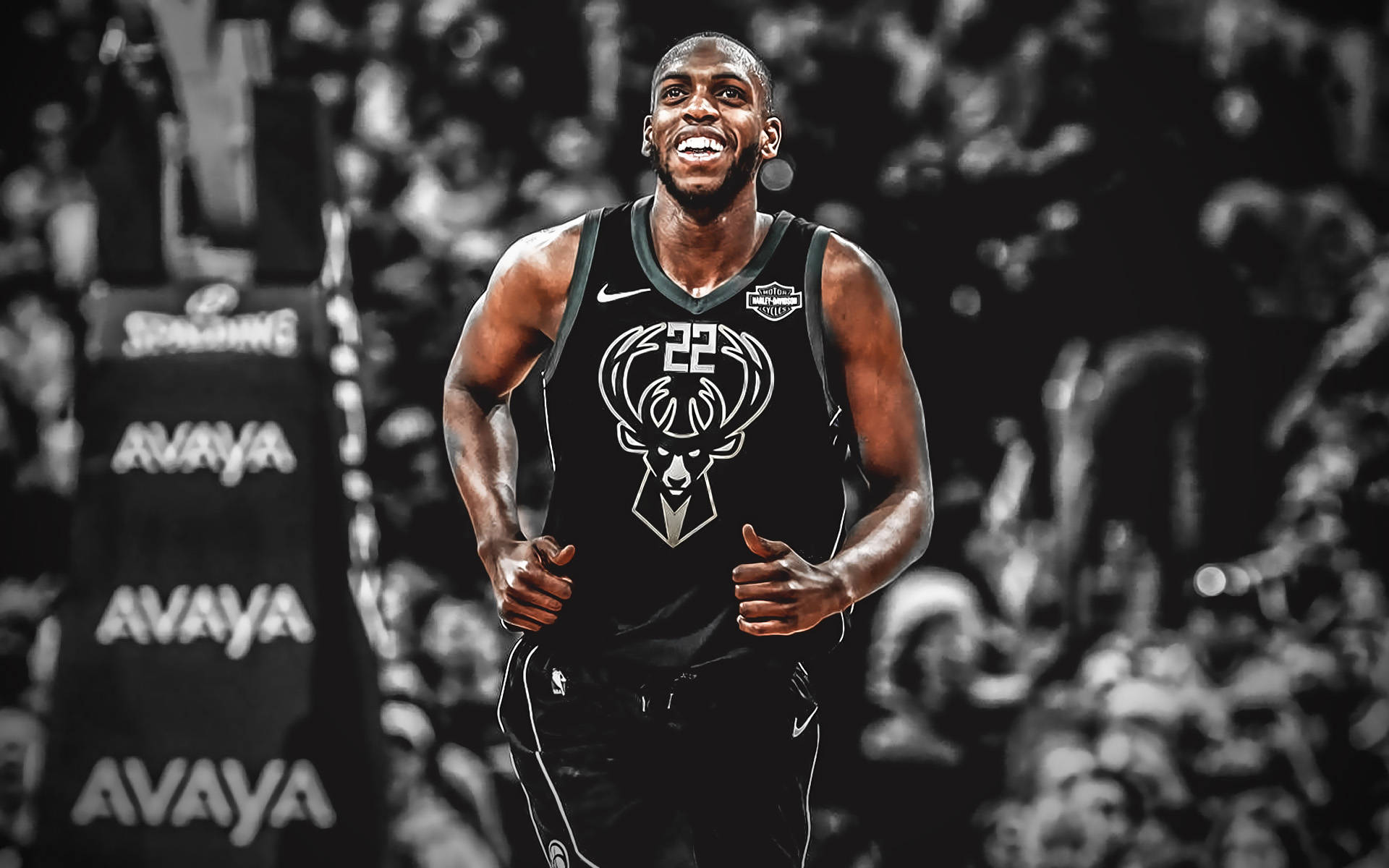 Khris Middleton 桌布 壁紙 — 一名身穿黑色密爾瓦基公鹿隊球衣的籃球運動員在球場上奔跑，背景有模糊的觀眾和AVAYA標誌，露出燦爛的笑容。