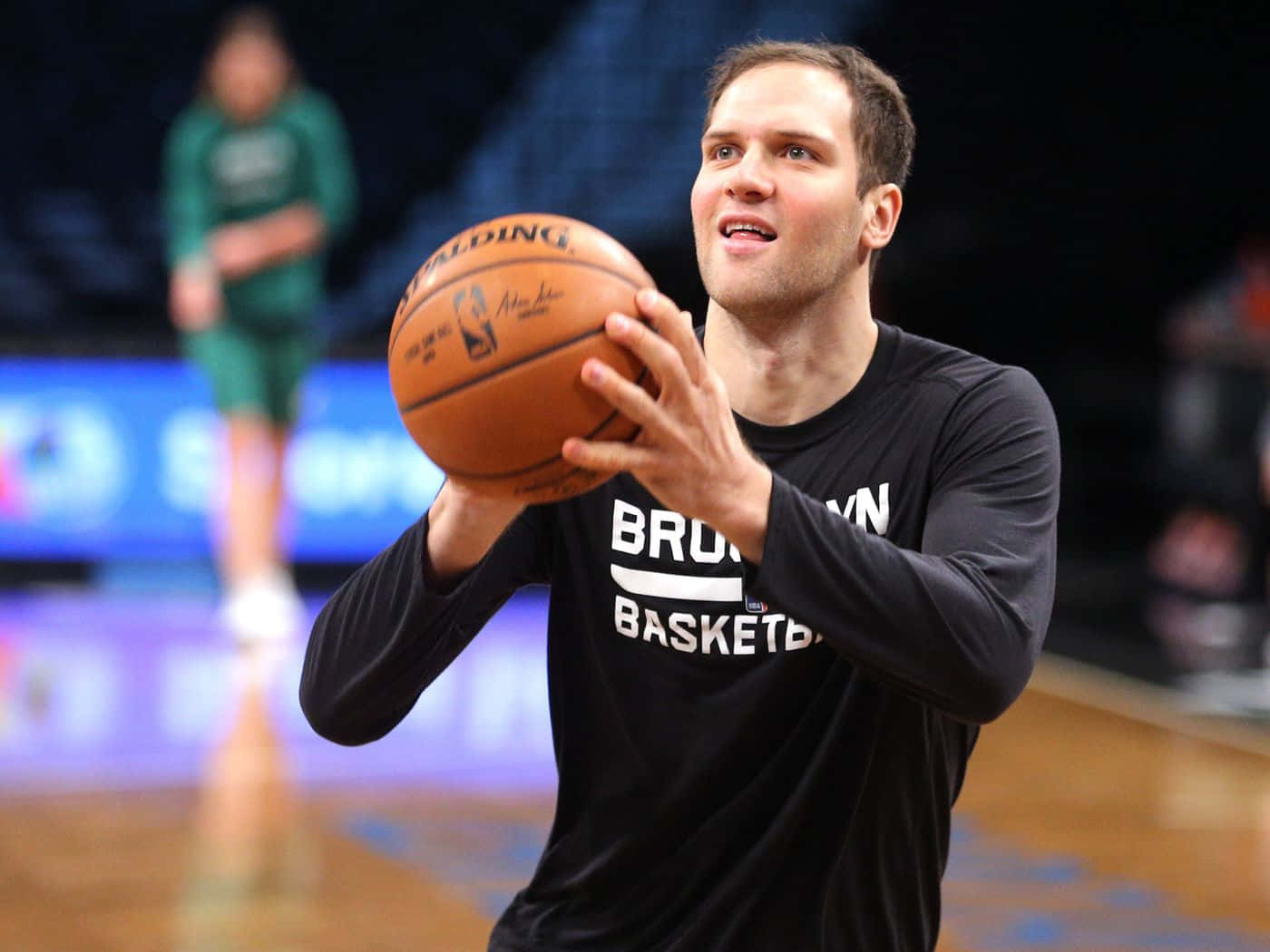 Brooklyn Nets 桌布 壁紙 — 一名身穿黑色布魯克林籃網球衣的籃球運動員，在明亮的場館燈光下，於拋光球場上準備投擲 Spalding 籃球。