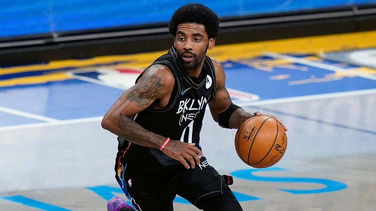 Kyrie Irving Nets 桌布 壁紙 — 一名身穿黑色布魯克林籃網球衣的籃球運動員，在明亮的場館燈光下，專注地在光滑的球場上運球。