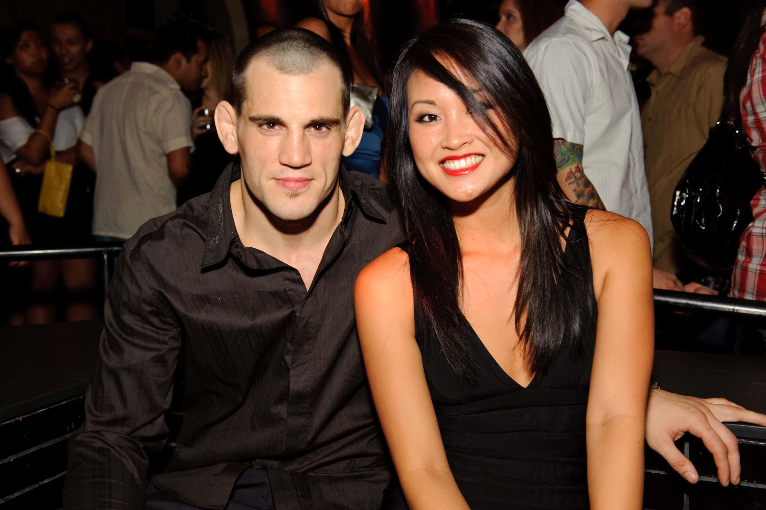 UFC 桌布 壁紙 — 一名身穿黑色服裝的男女在燈光昏暗、擠滿人群的派對場景中對著鏡頭微笑。